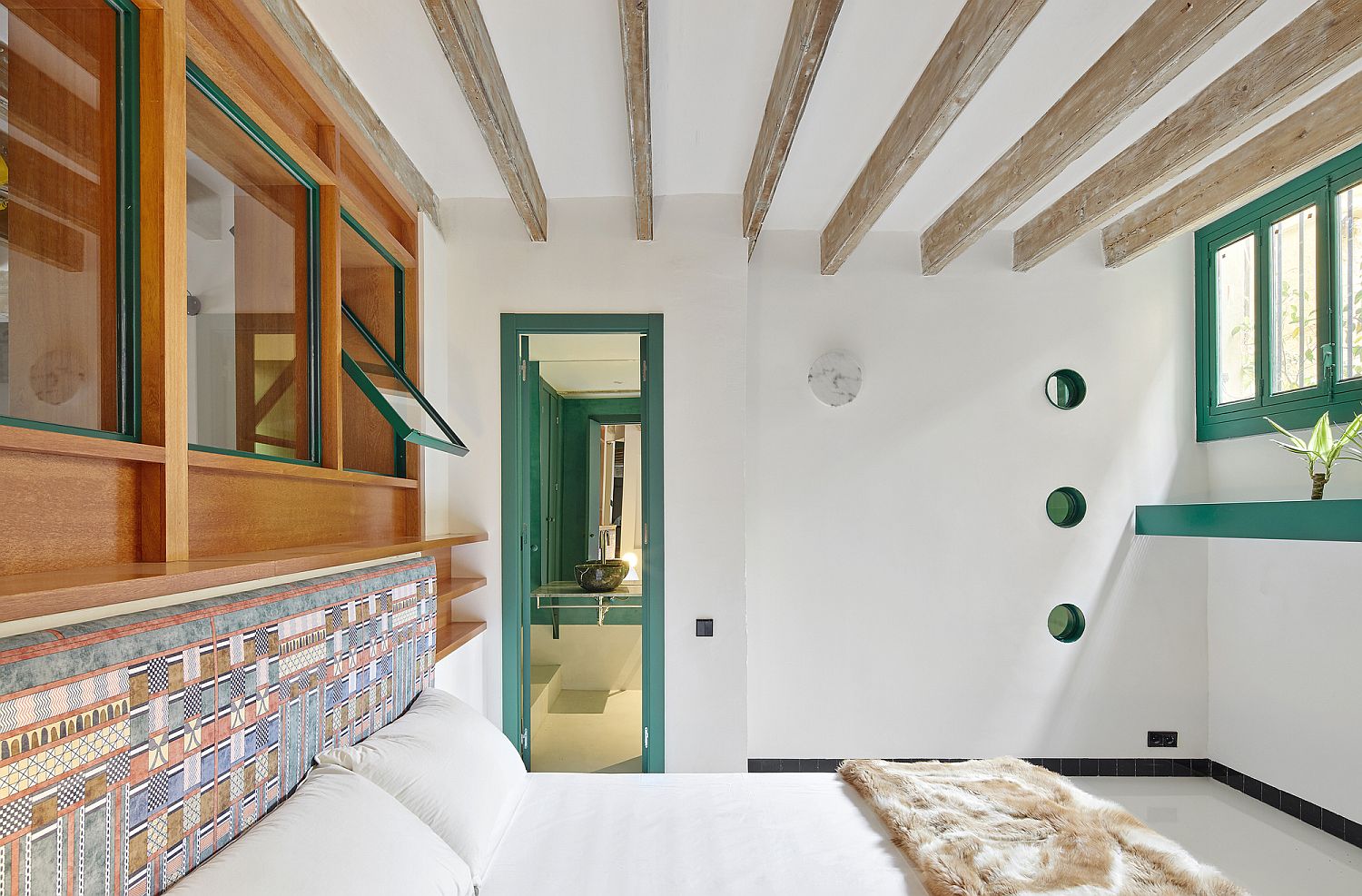 Bedroom in white with built-in shelving, green window frames and ceiling beams