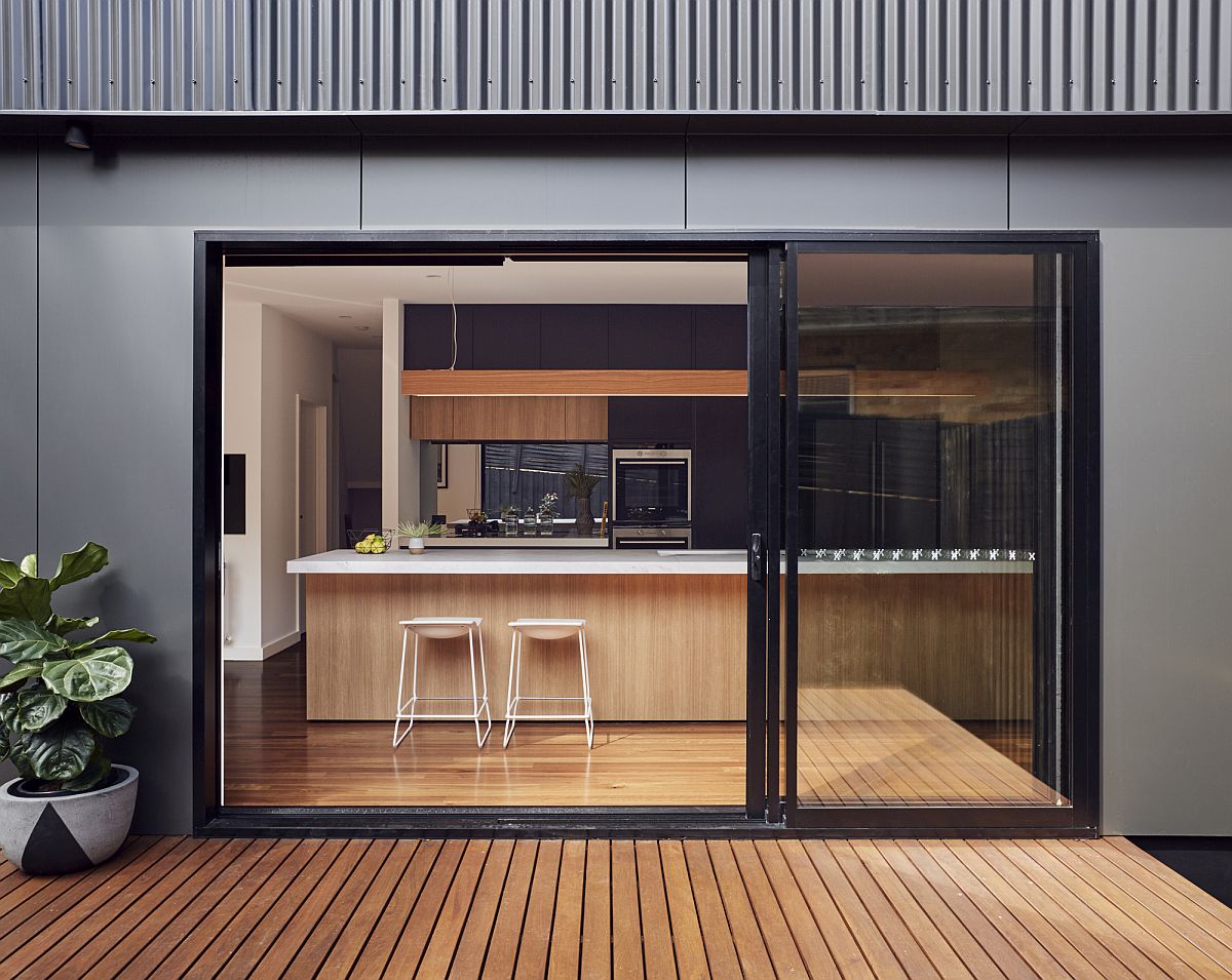 Sliding glass doors with drak frame connect the interior with the wooden deck