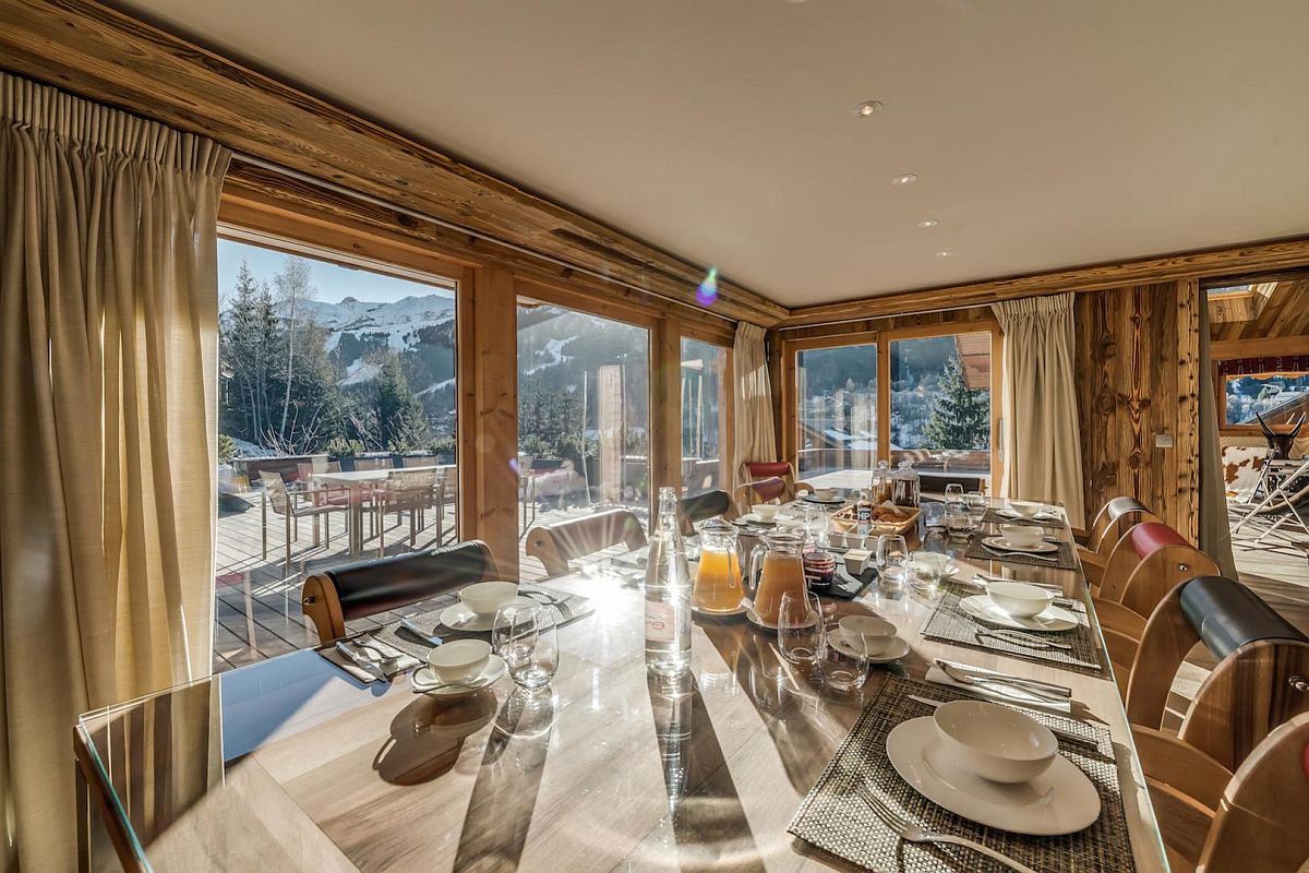 Formal dining room of luxury chalet with large glass walls and Alpine views