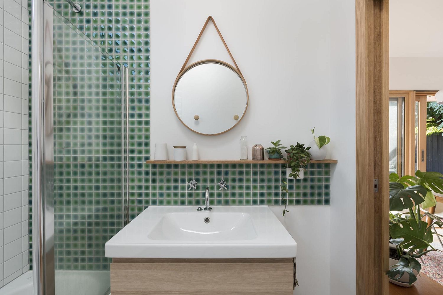 Small green tiles in the bathroom along with a small vanity and stylish mirror