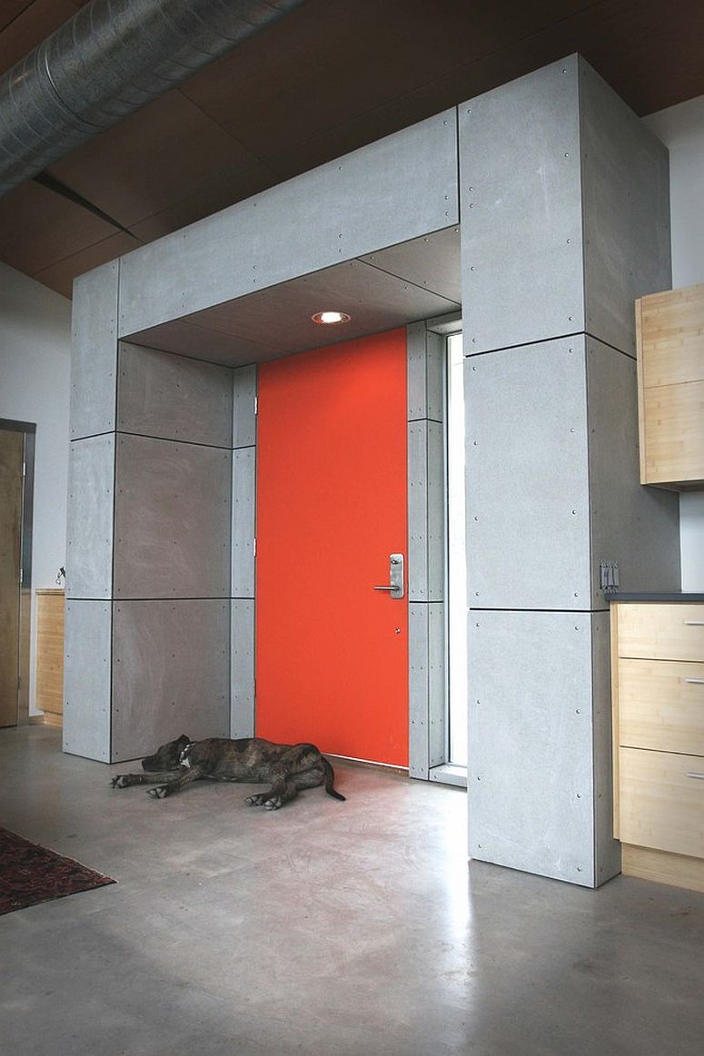 Industrial style entry with exposed concrete, duct pipes and a splash of bright orange