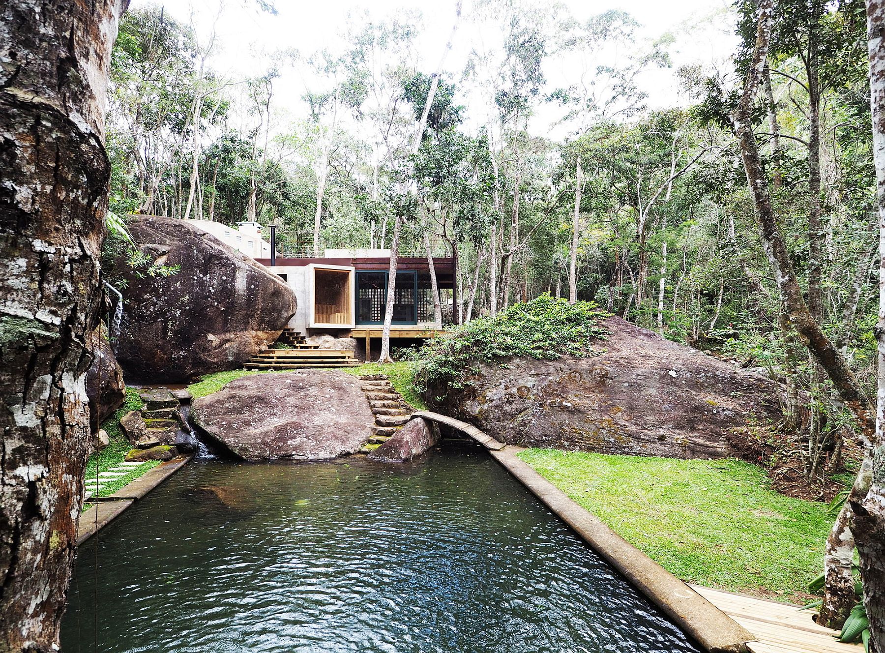 Modern pavilion set next to a natural swimming pool surrounded by lush green landscape