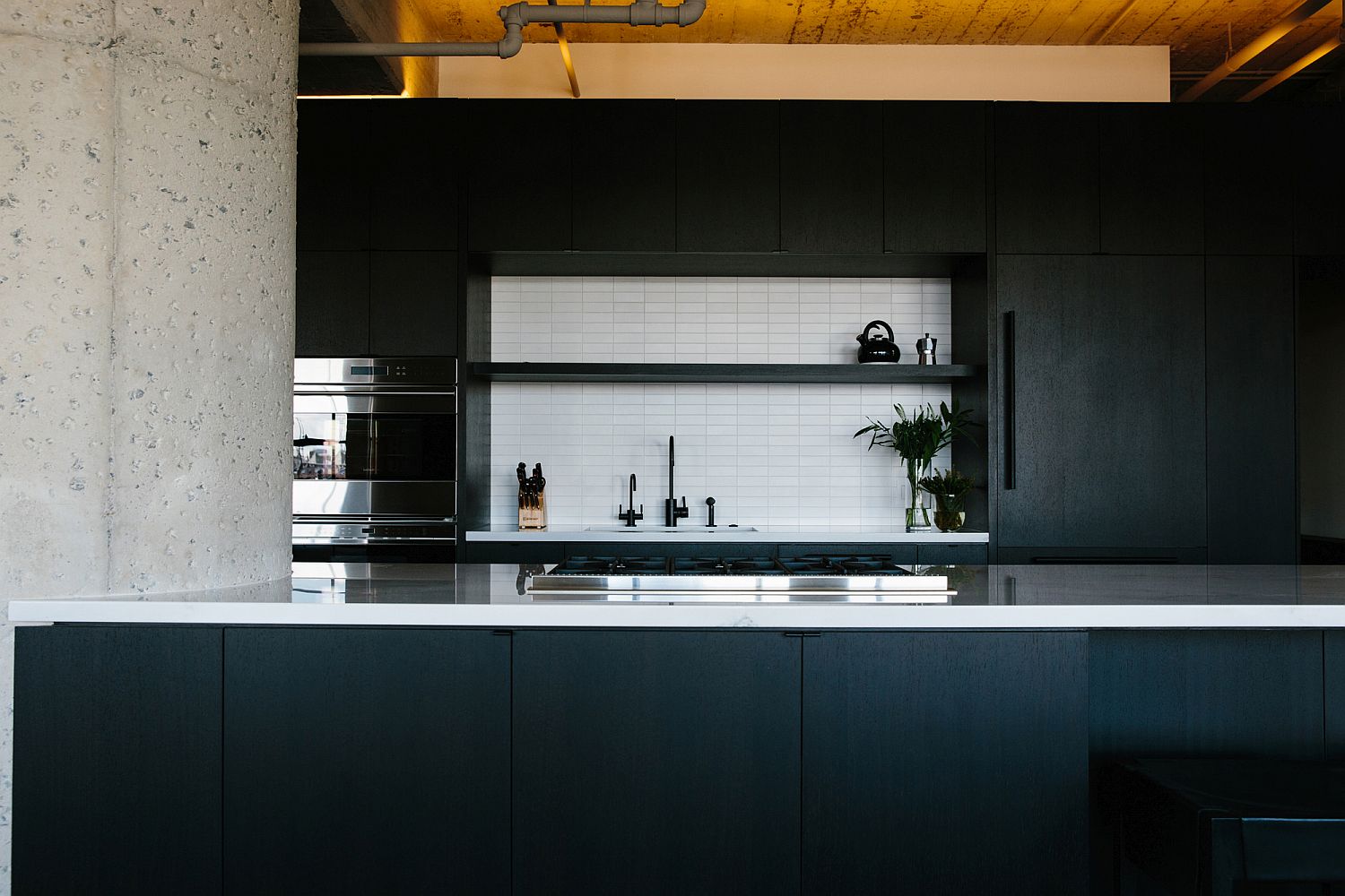 White backsplash stands out in the kitchen thanks to black cabinets and dark gray island