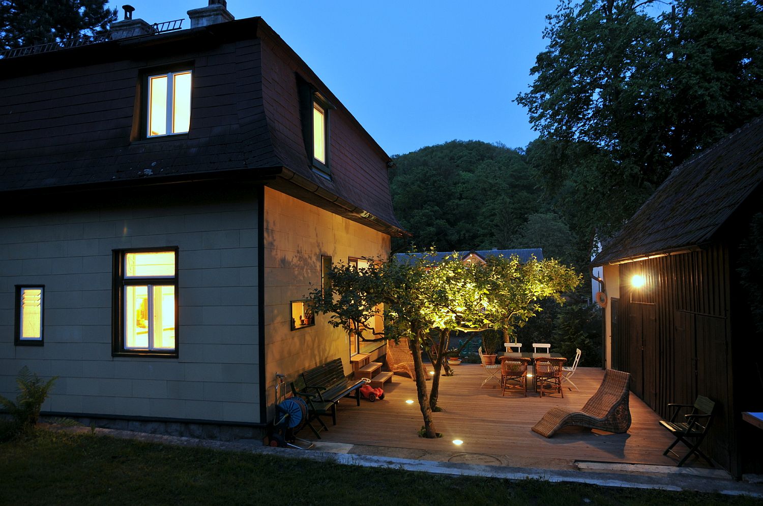 Gorgeously illuminated larch deck with cut outs for trees connects the home with the new backyard escape