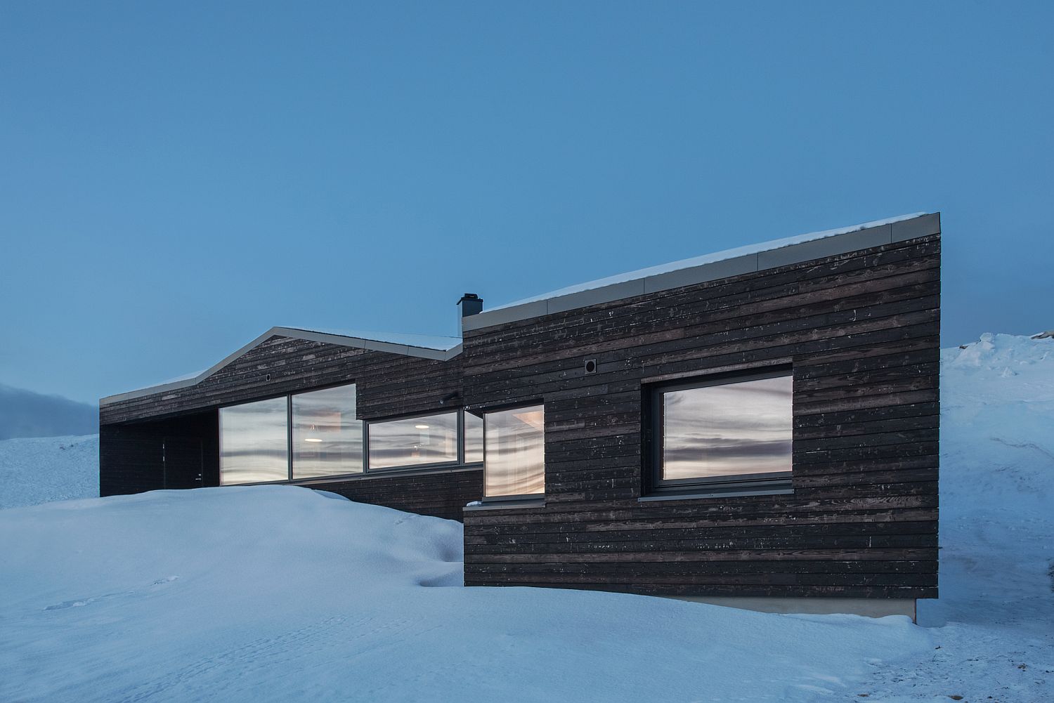 Minimal and striking exterior of the Norwegian cabin on snowy slopes