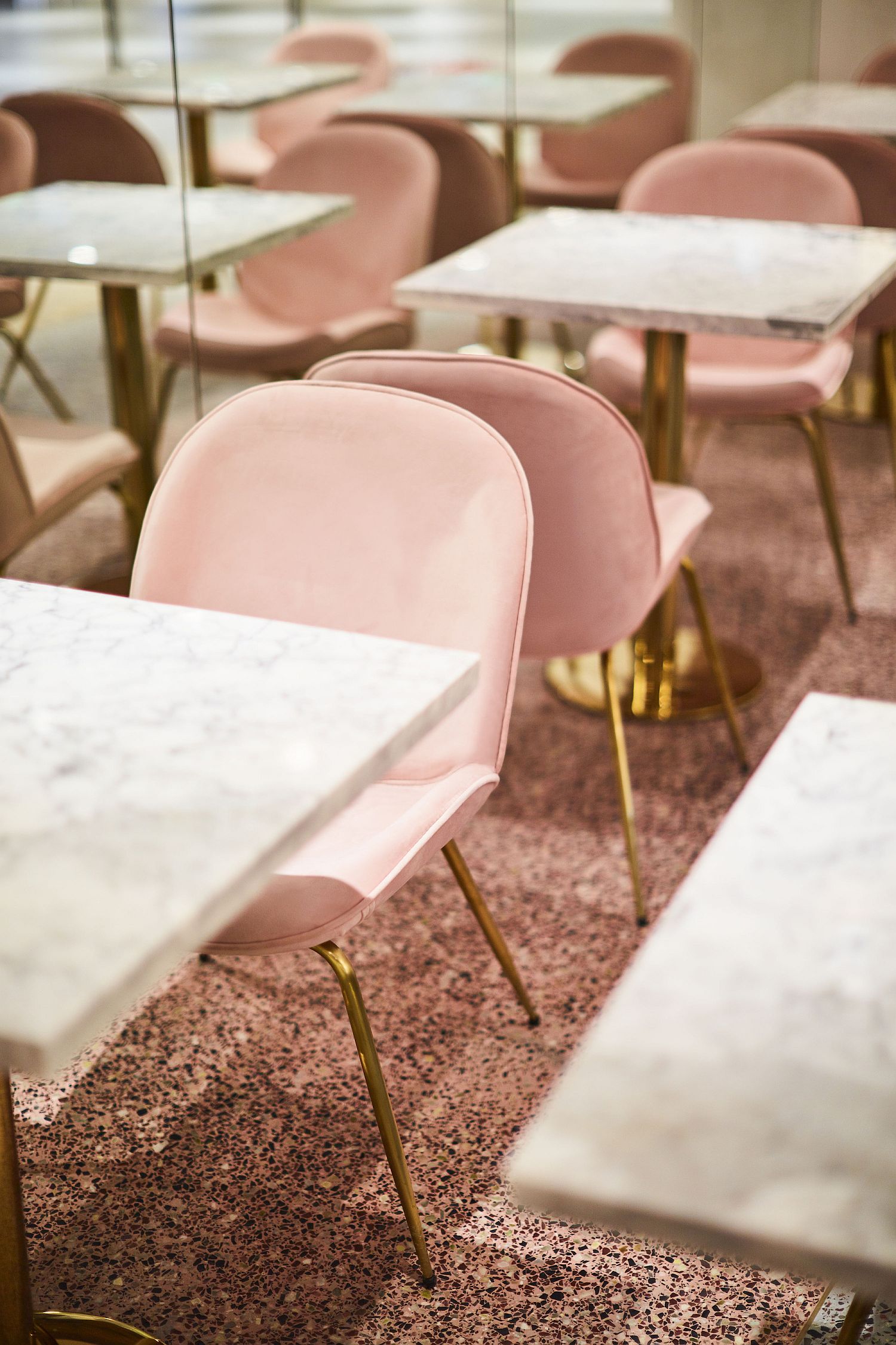 Marble top dining tables with metallic legs and pastel pink chairs next to them