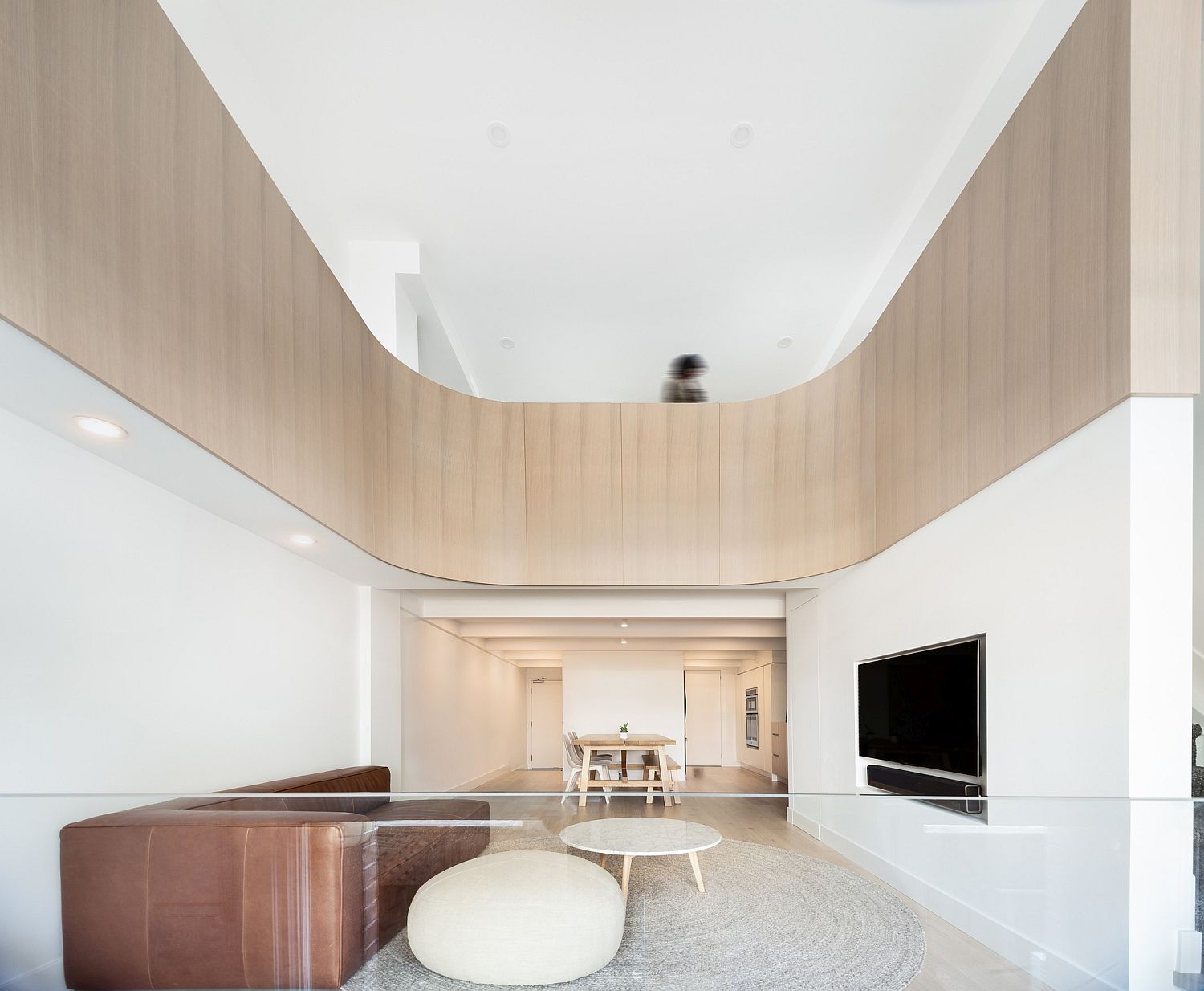 Curved wooden section gives the double height minimal living room plenty of visual warmth