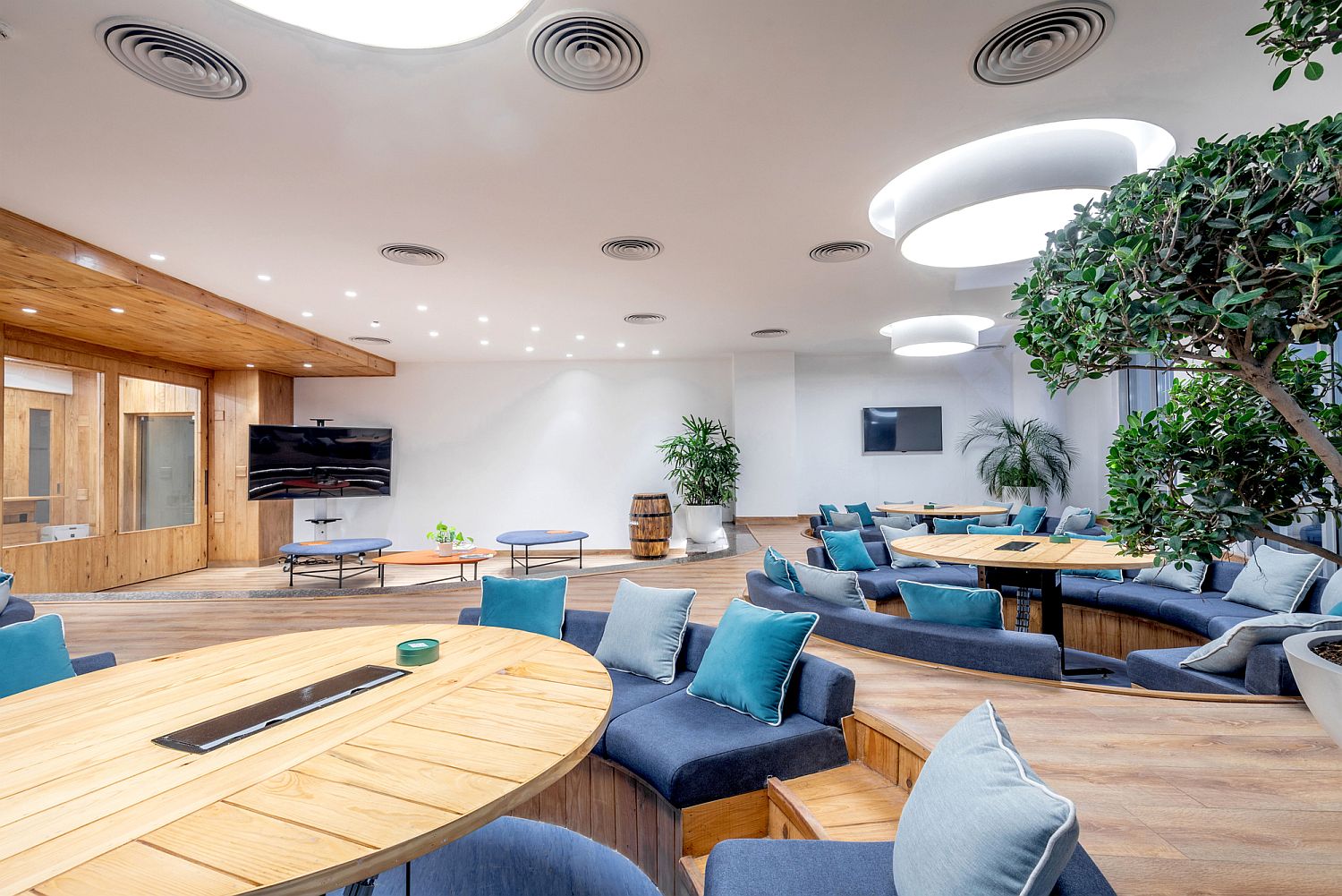 Circular wooden tables with tech-savvy design sit inside teh comfy sunken conversation zones