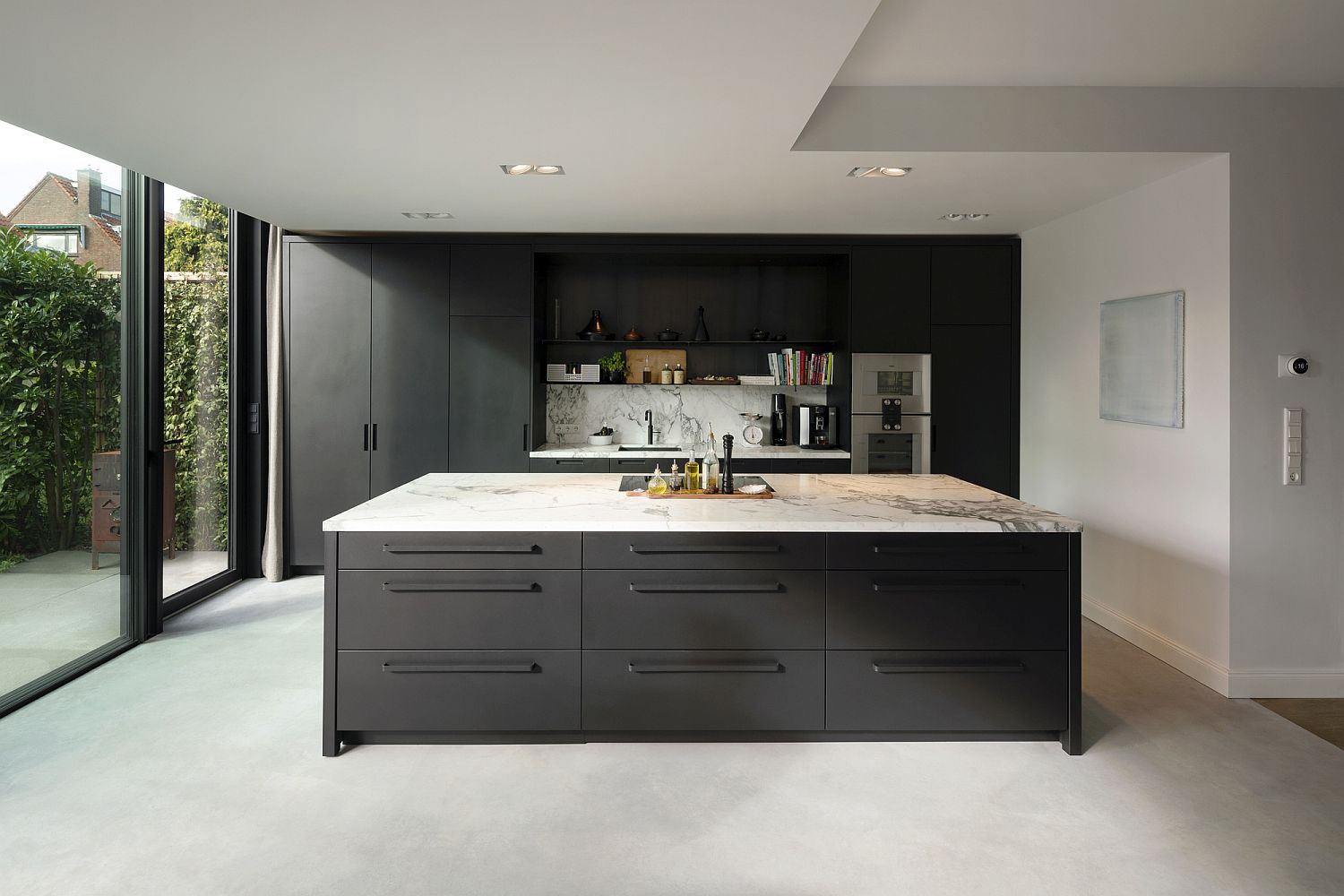 White kitchen with marble countertops and dark island along with dark gray shelving