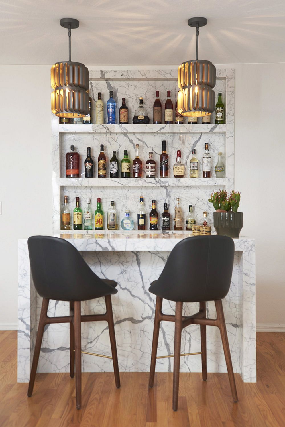 Home bar with marble backsplash and counter along with a couple of bar stools