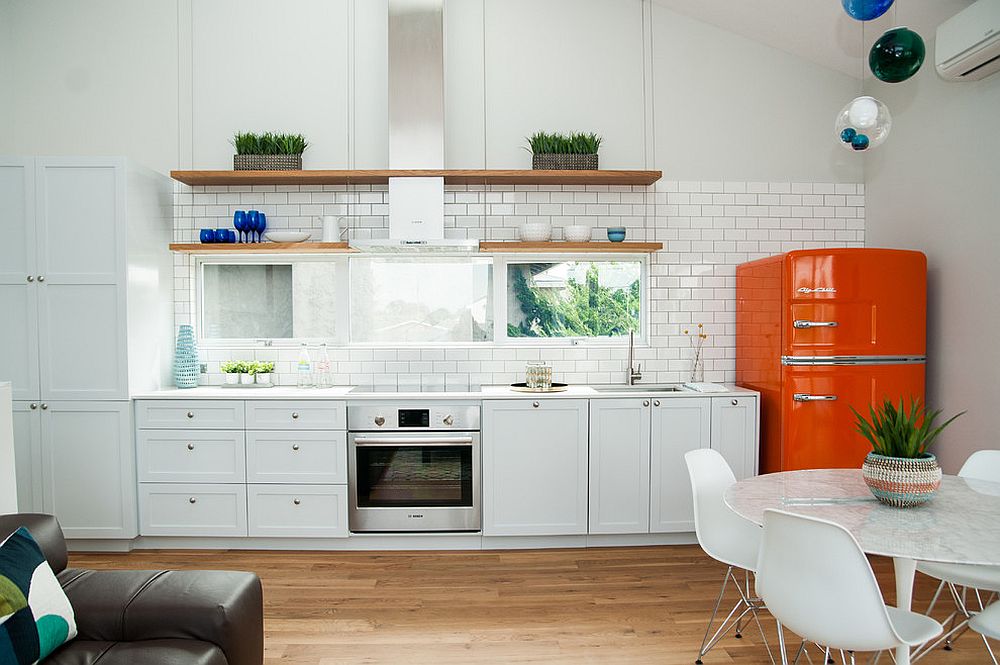 Bright orange refrigerator adds color to the white beach style kitchen