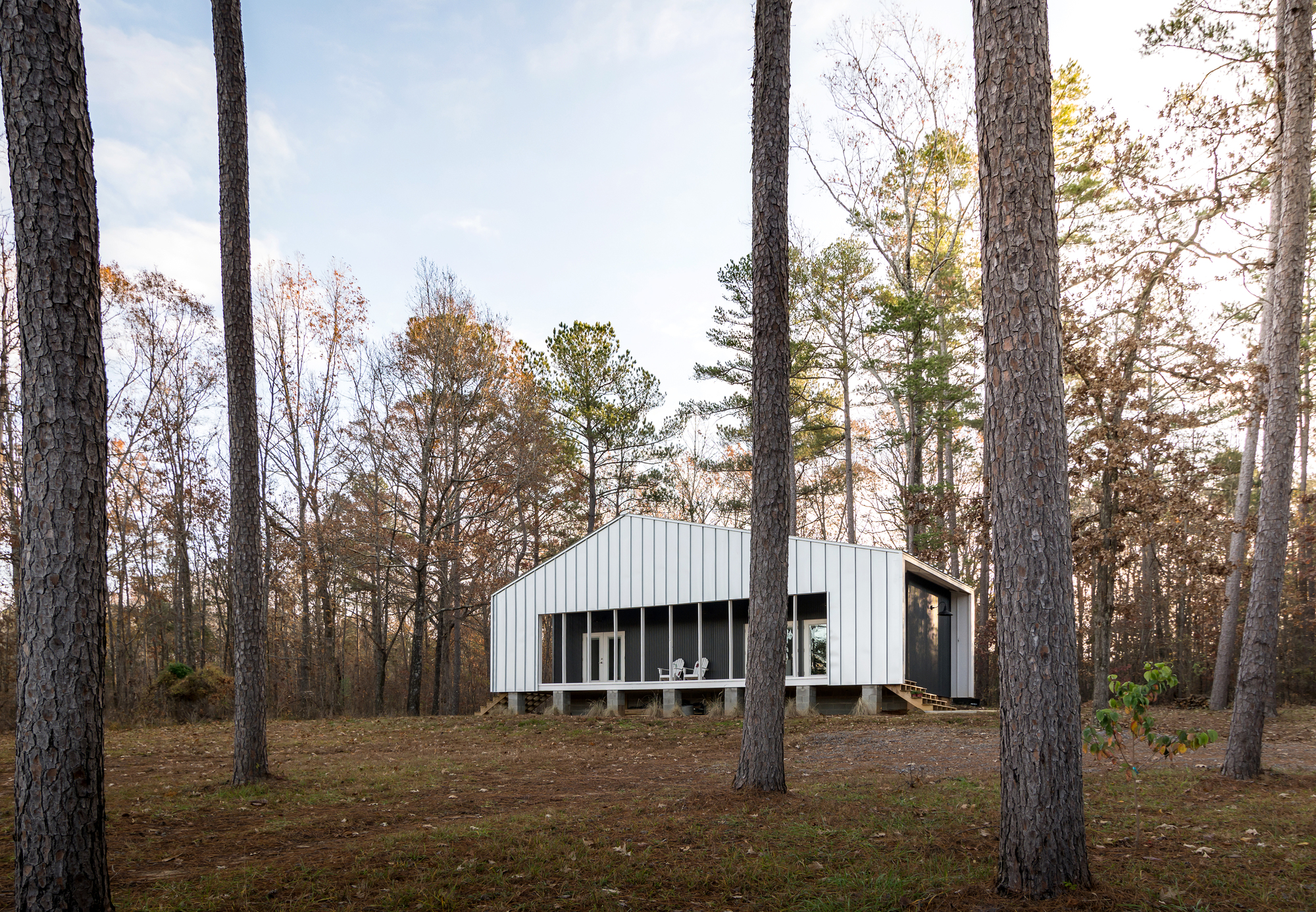 Woodsy exterior of the house in white reflects the rustic style of the backdrop beautifully