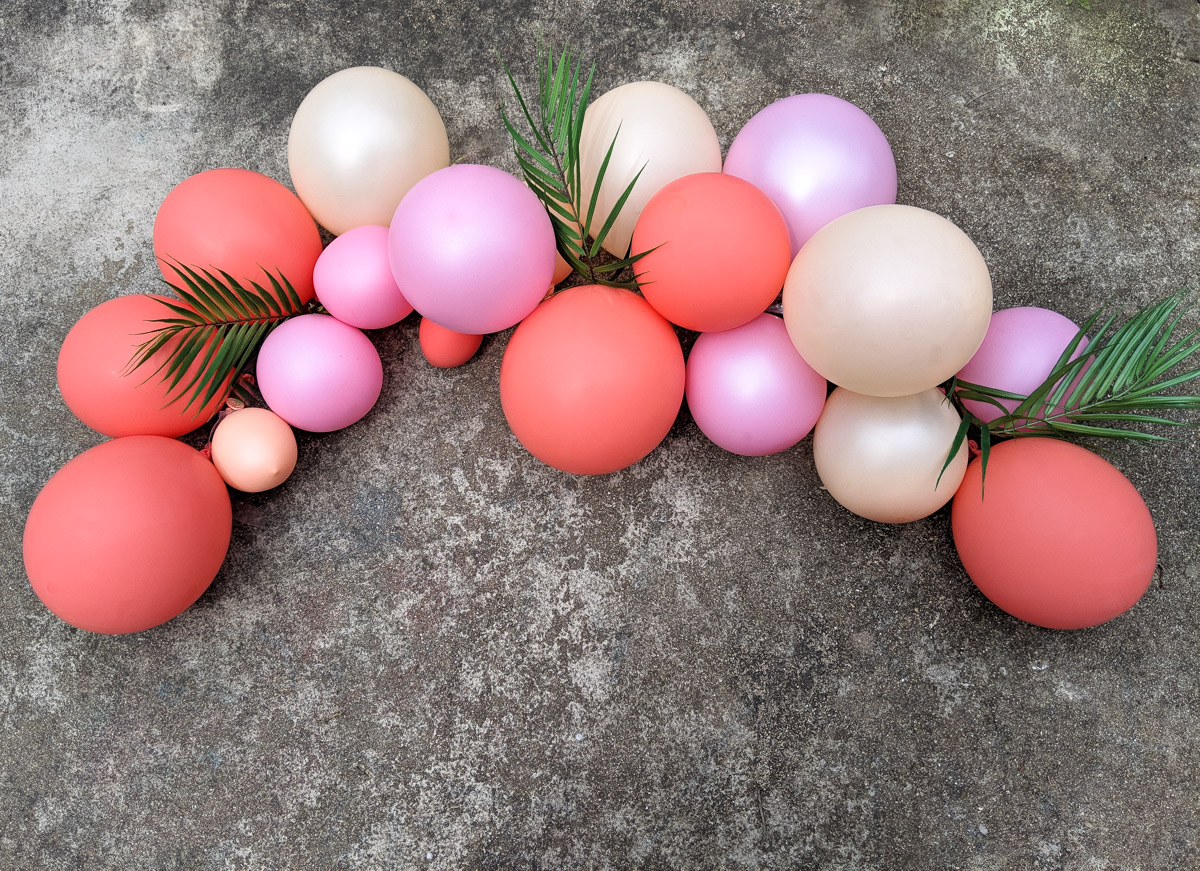 Pink-toned balloon arch with tropical greenery