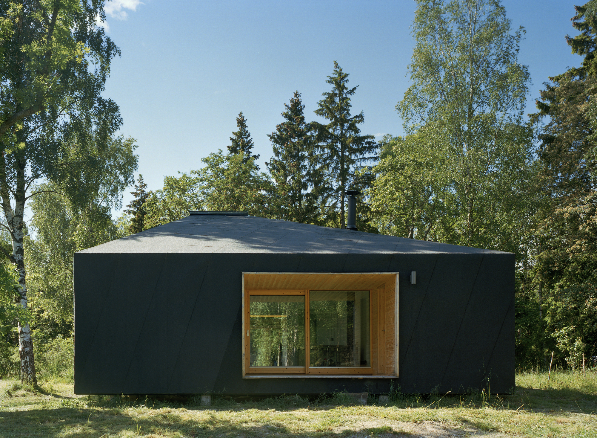 Dark exterior of the small summer house in woods allows it to blend in with the backdrop