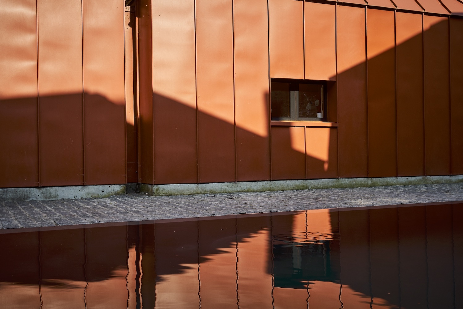 Metallic orange exterior of the house is reflected in the pool