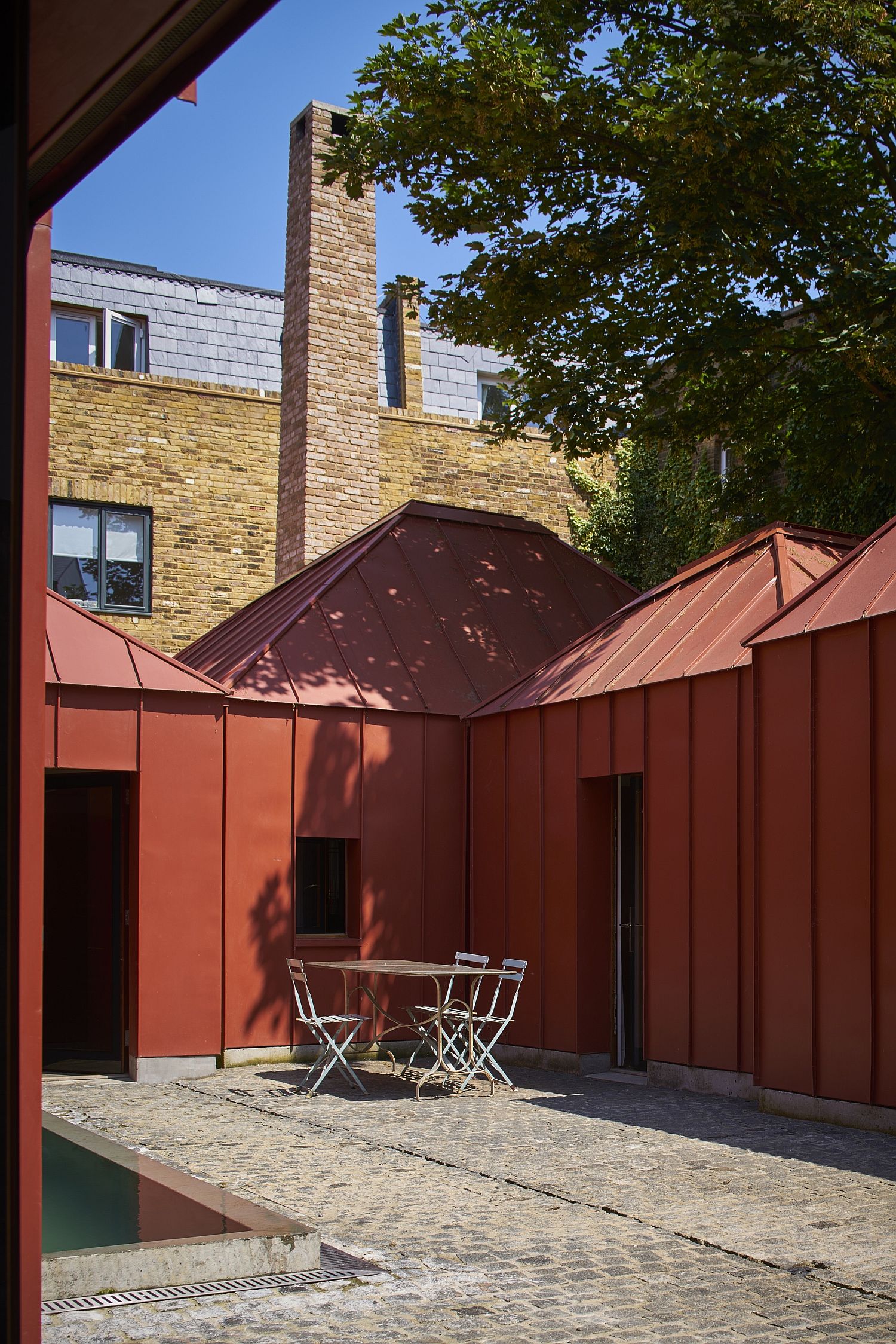 Multiple pavilions in orange metal create a cool courtyard within