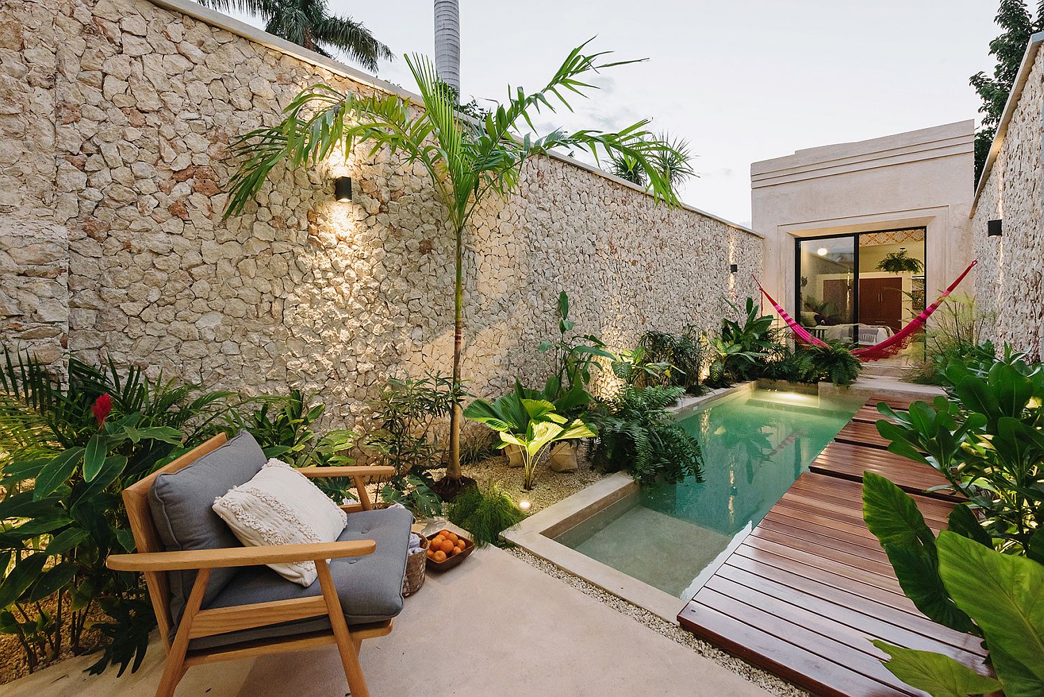 Stone wall, lush green vegetation and a slim wooden deck create a private and relaxing pool zone