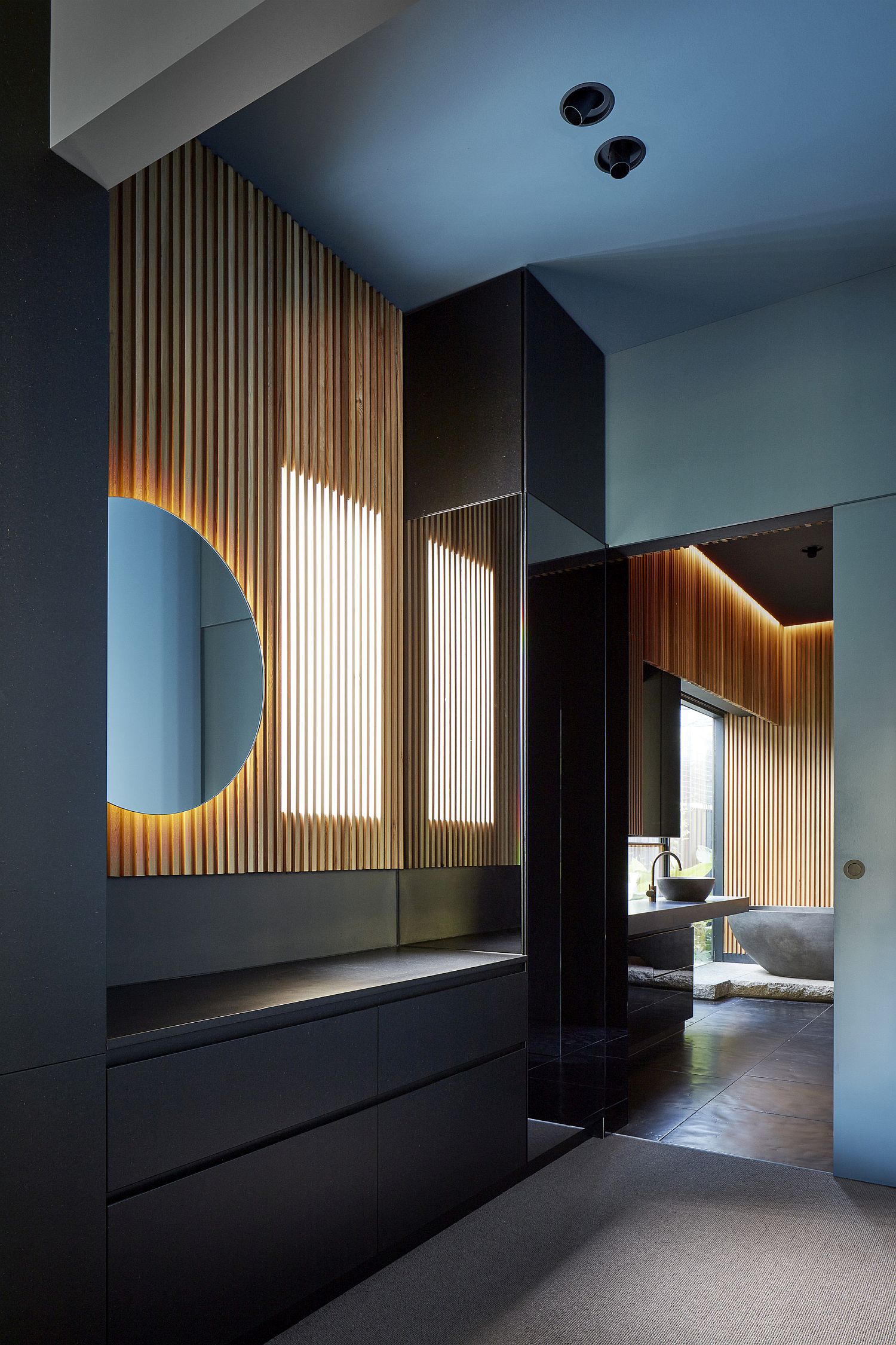 Wooden slats and round mirror accentuated by brilliant use of lighting