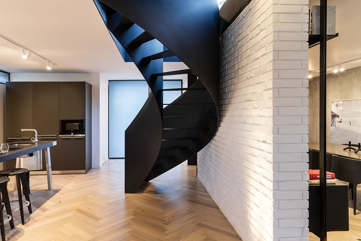 Brick wall divides the lower level of the house and offers white backdrop for the spiral staircase in black