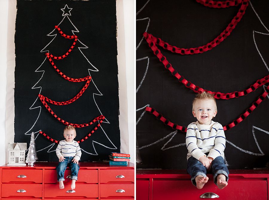 Chalk drawn Christmas tree on a black board, fronted by a child sitting on a red dresser. 