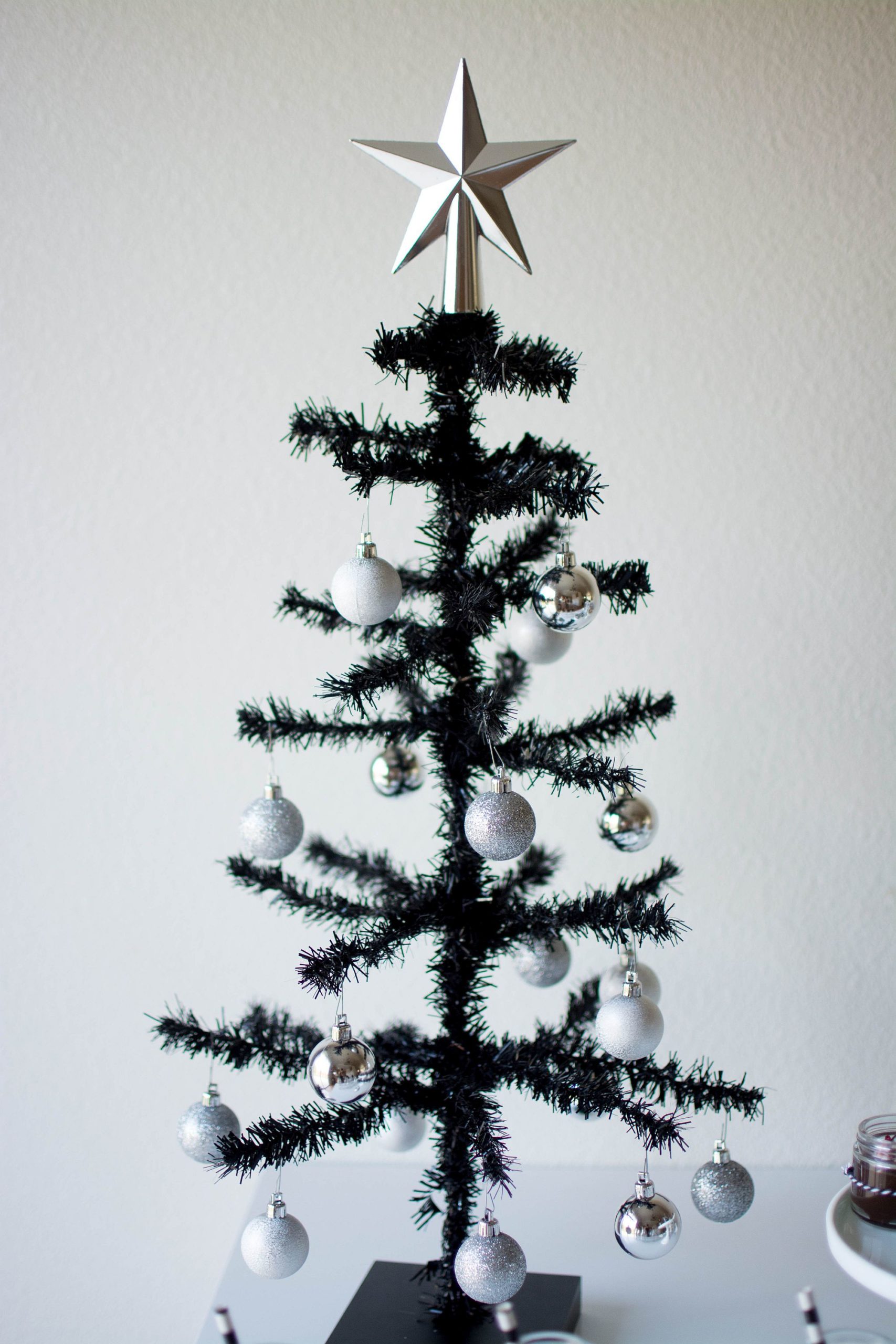 A thin black Christmas tree with silver star topper.