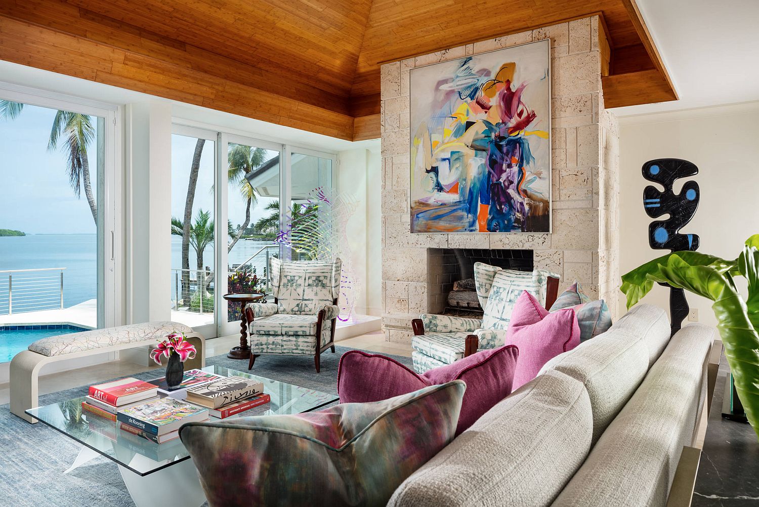 Fireplace with colorful wall art sits at the heart of the breezy tropical living room of Miami Home