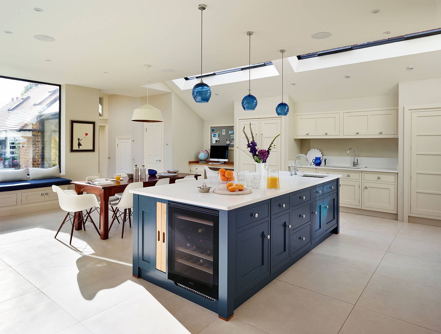 Kitchen in white with blue island that features wine storage space, blue pendants and skylights