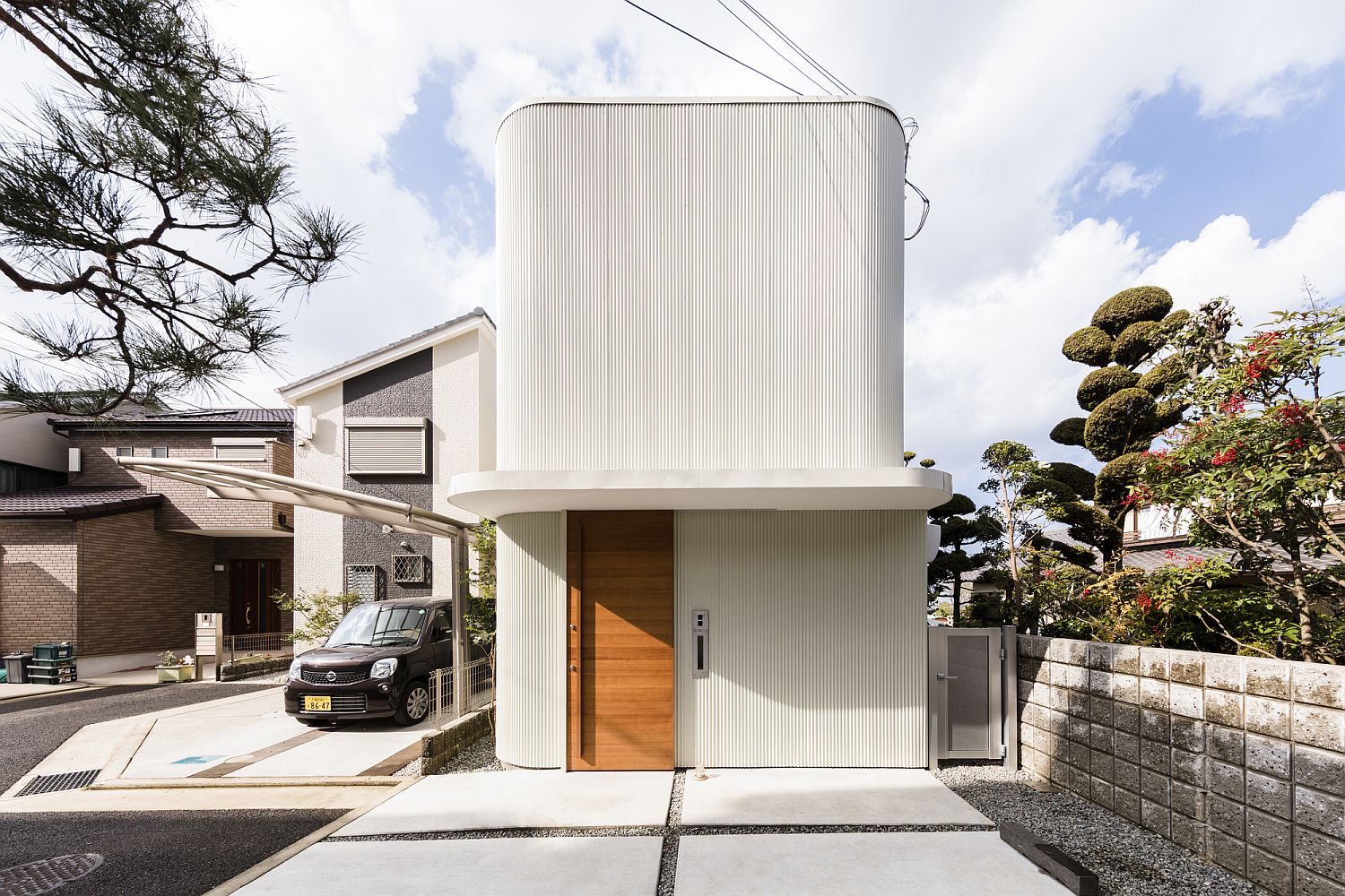 Street facade in white wth curved walls and a wooden entrance door of home in Japan