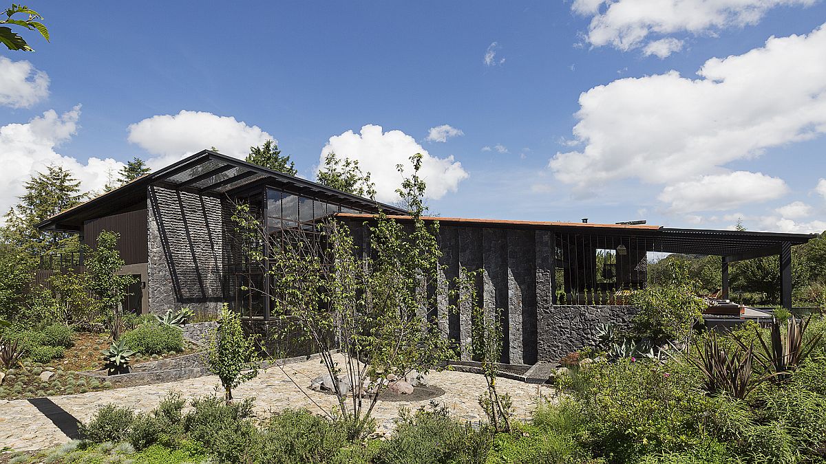 Slanting roof forms and stone wall made from dark, locally sourced volcanic rock for the Mexican Weekend home