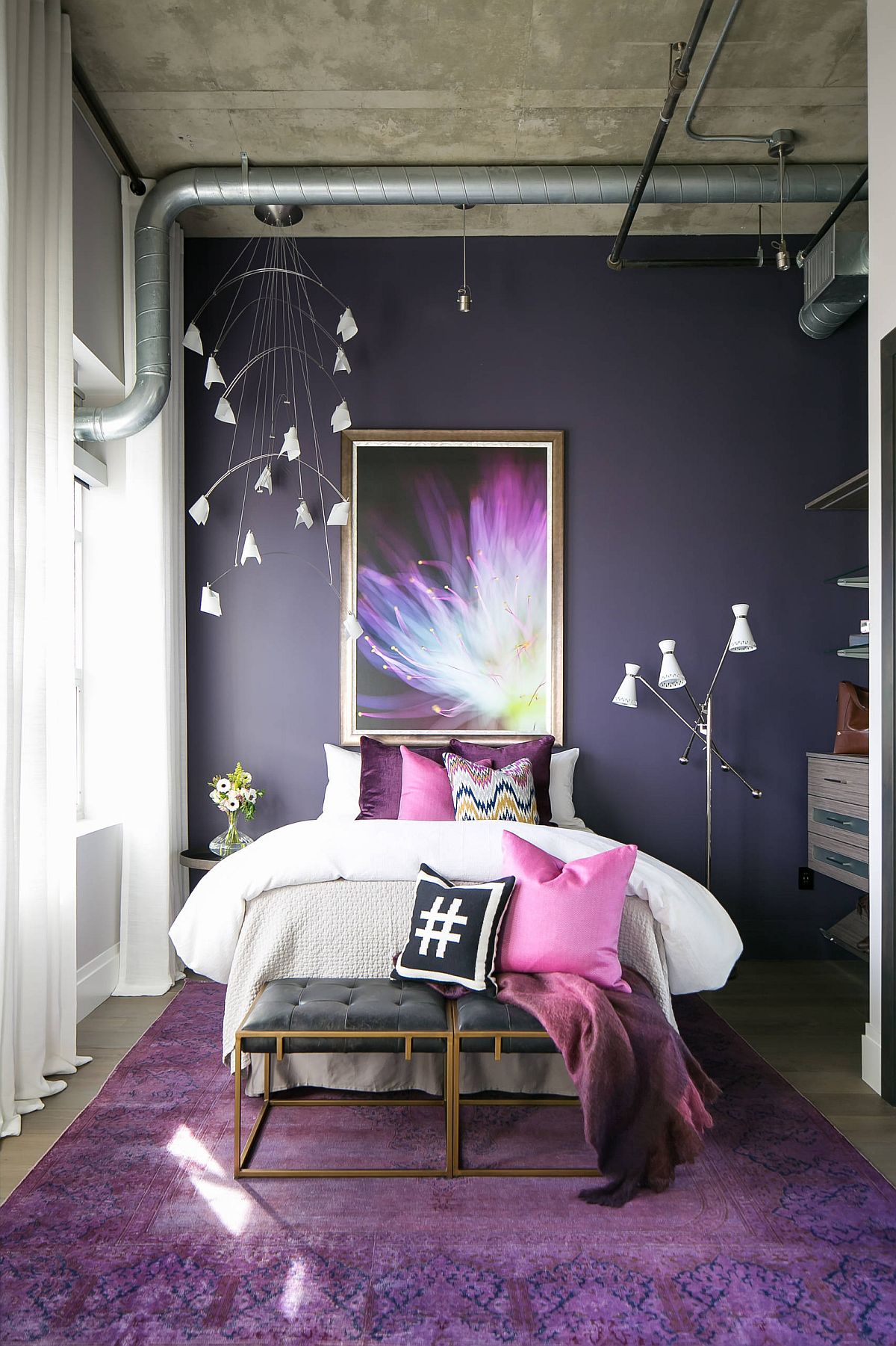 Concrete ceiling and exposed duct pipes bring industrial beauty to this colorful bedroom in violet