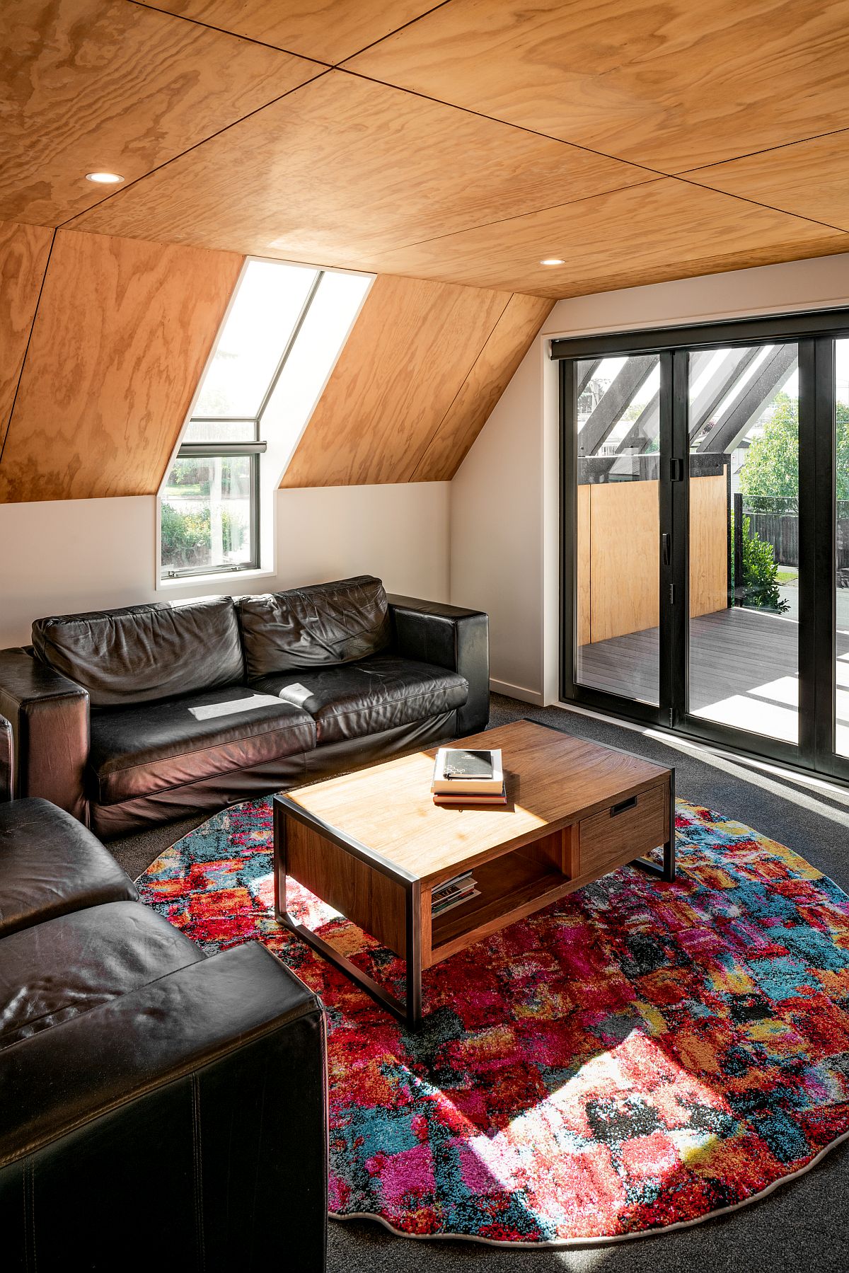 Cozy attic style living area with comfortable seating, wooden ceiling and a colorful rug