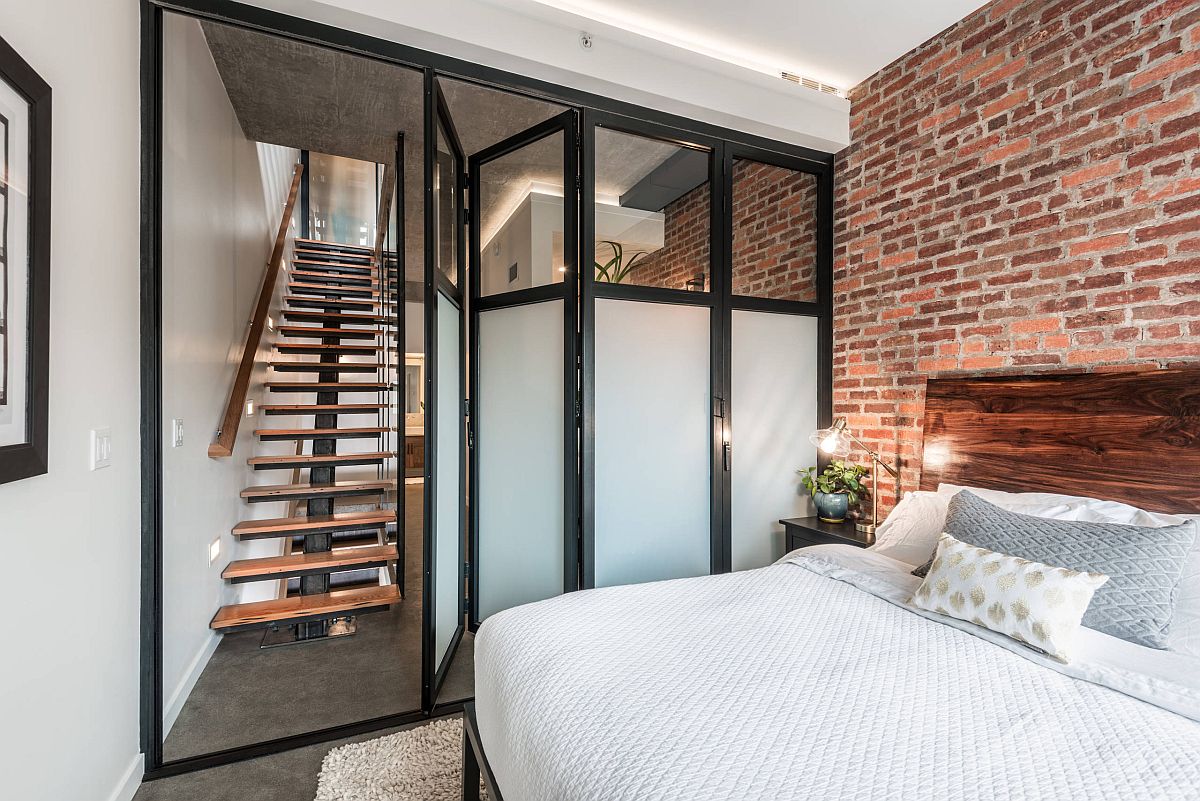 Folding doors and a neutral backdrop add to the spacious design of this small industrial bedroom with accent brick wall