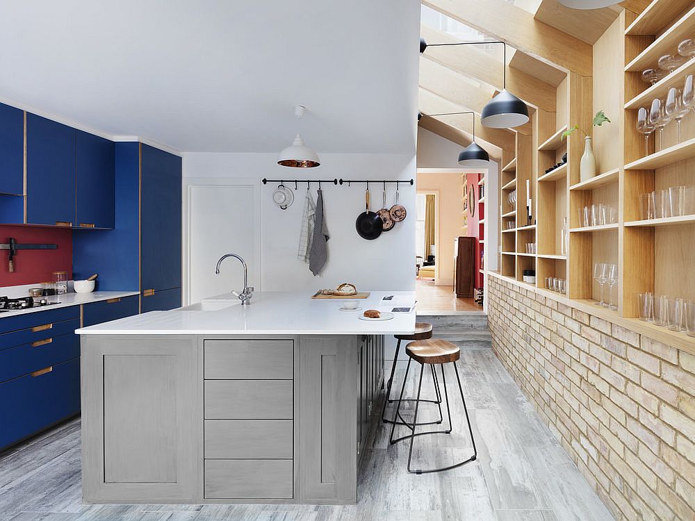 Gorgeous blue cabinets add color and contrast to the neutral kitchen with brick walls and wooden shelves