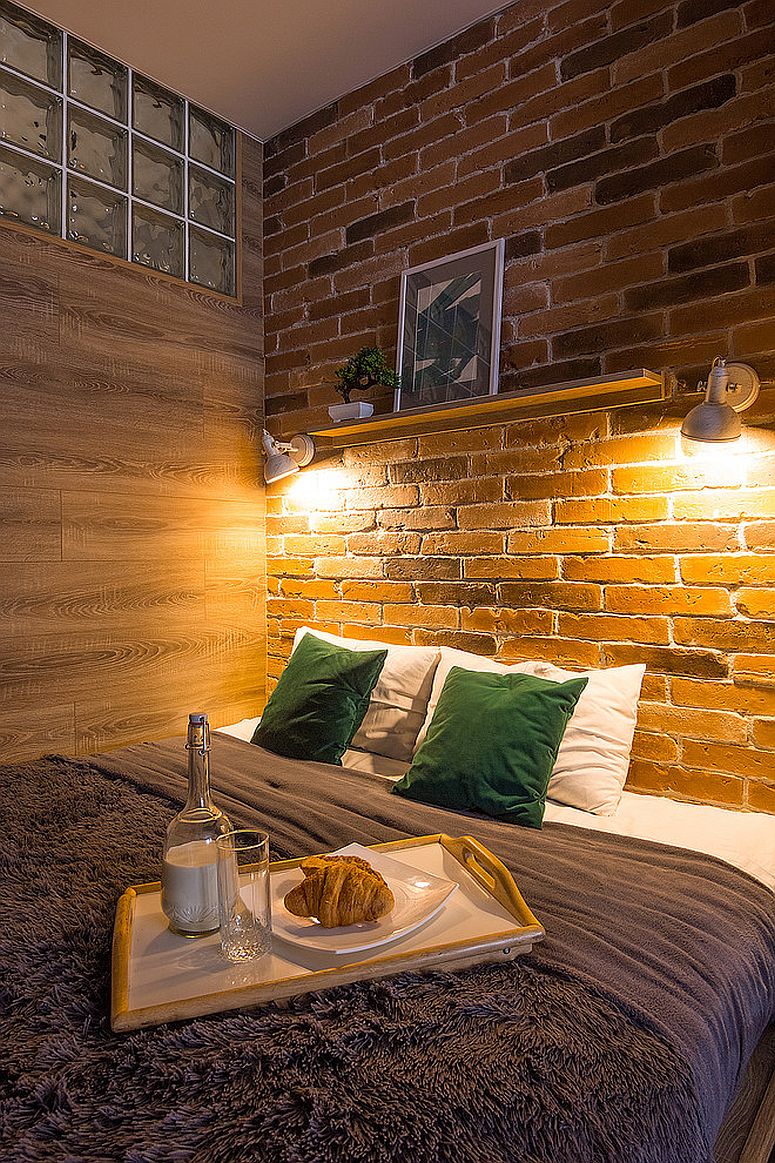 Sconce lighting illuminates the headboard brick wall in the small industrial bedroom