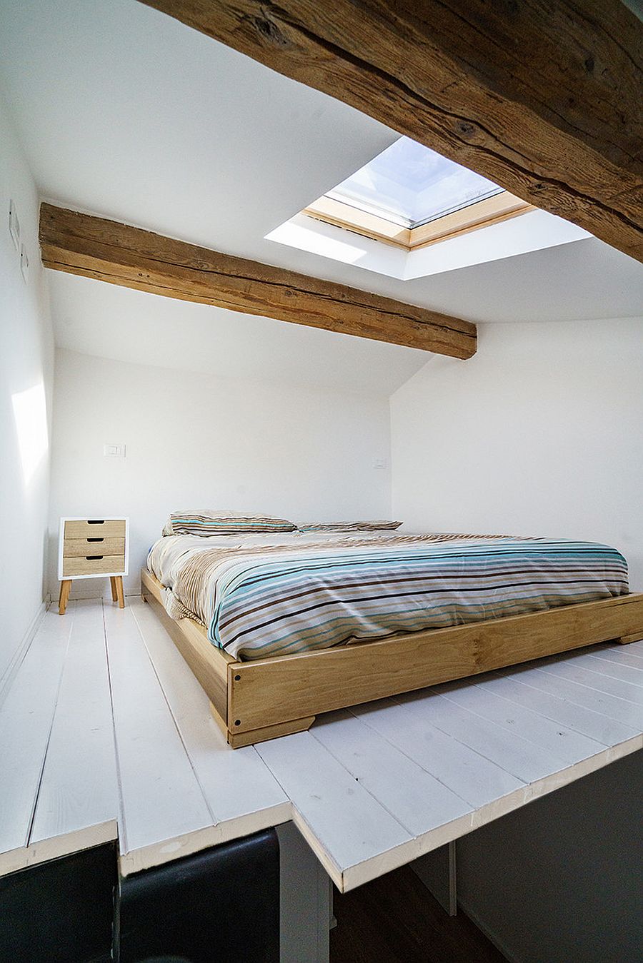 Skylight brings natural light into the tiny attic level industrial bedroom in white