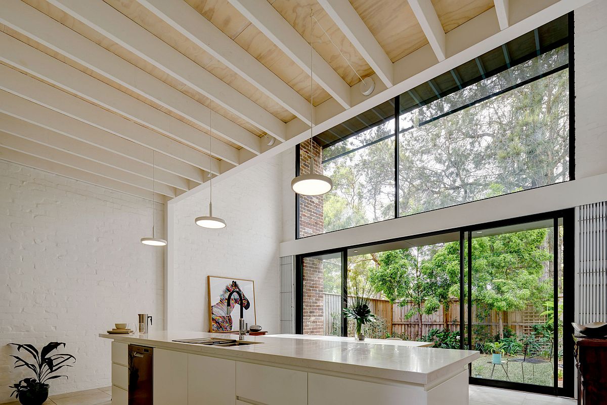 Sliding glass doors and glass walls connect the white modern kitchen wih the rear yard