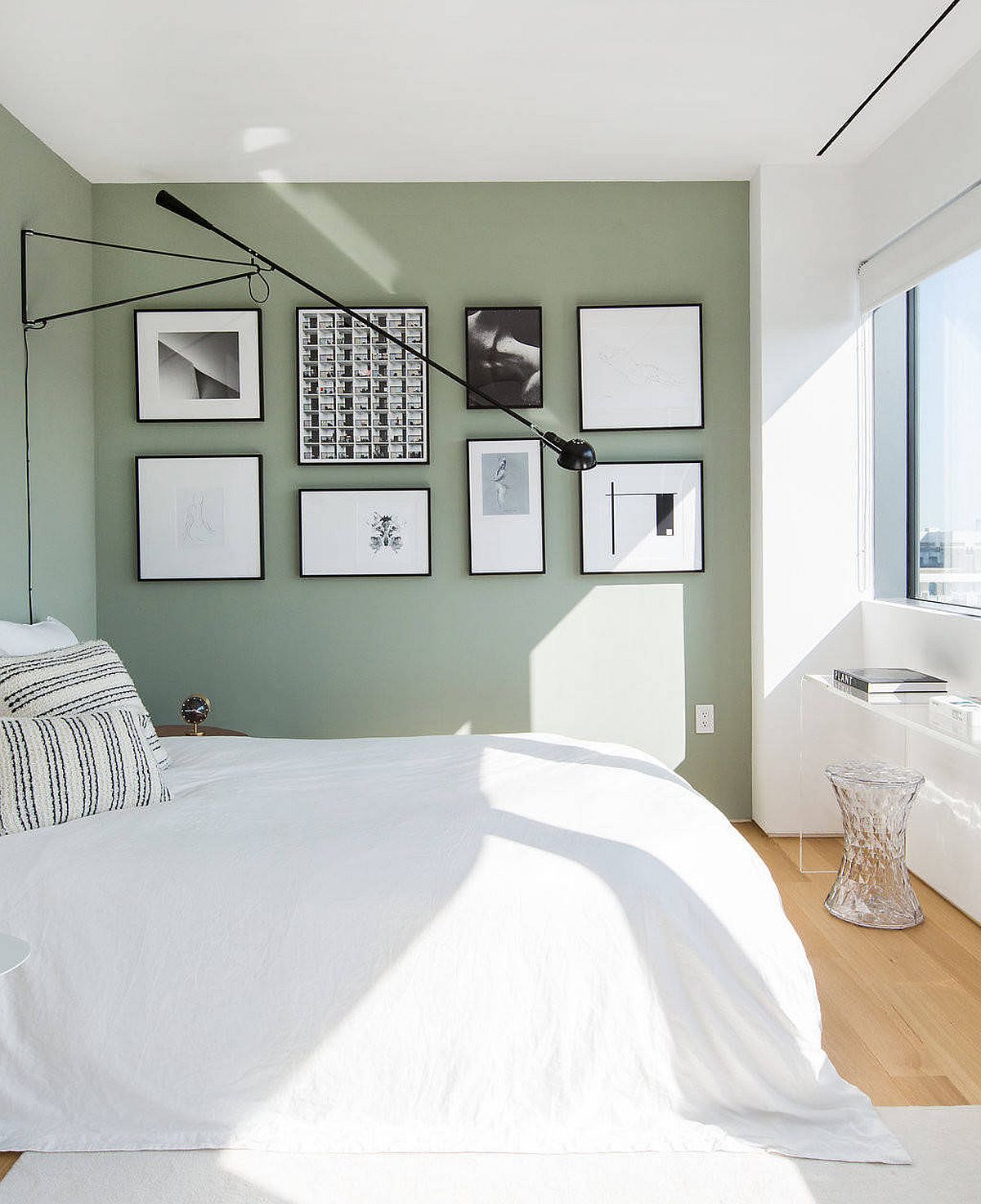 Gallery wall with black and white photographs set against a pastel green wall steals the show in this bedroom of New York home