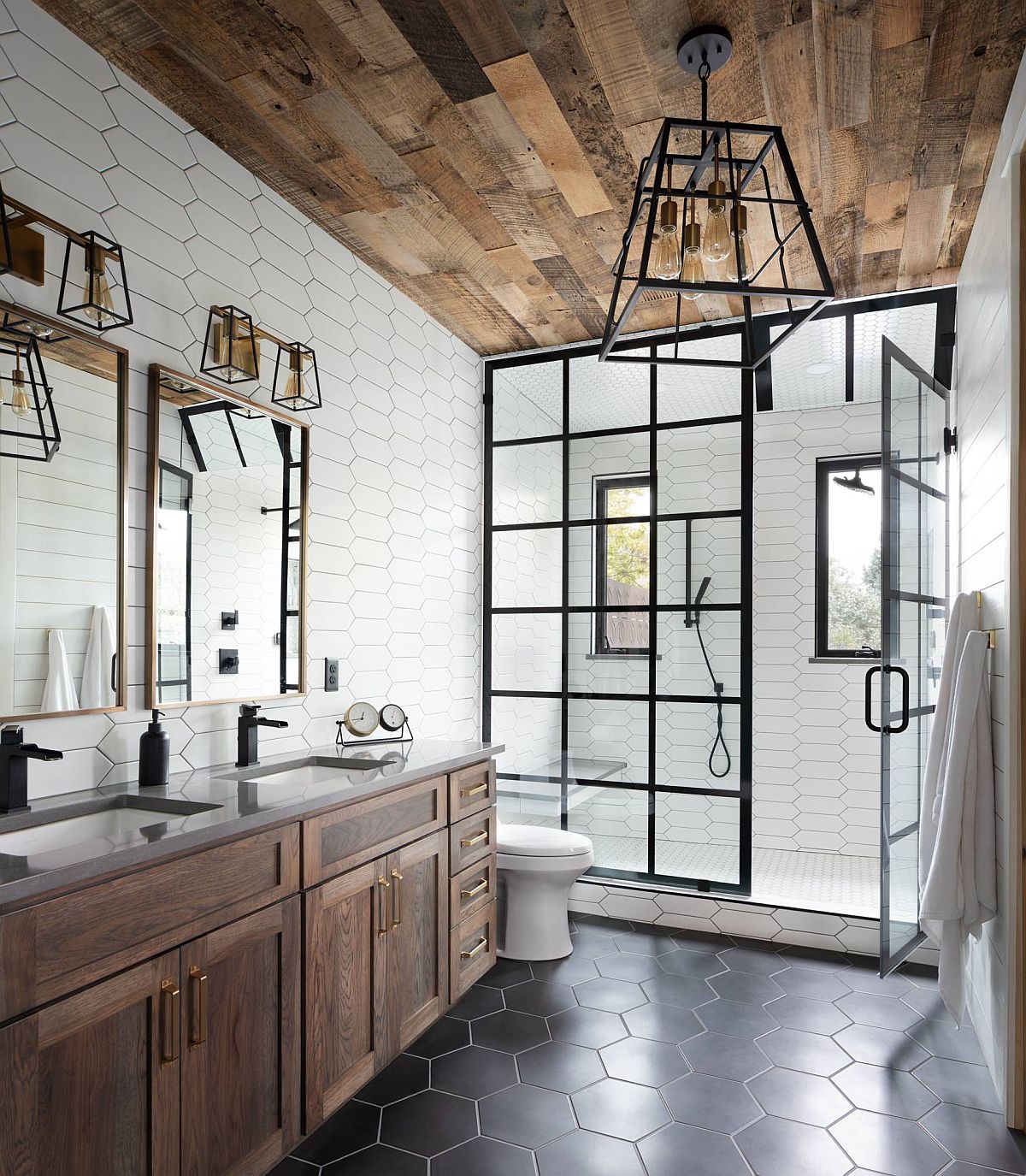 Gorgeous industrial farmhouse style bathroom with hexagonal gray floor tiles. wooden ceiling and lovely dark-framed shower area