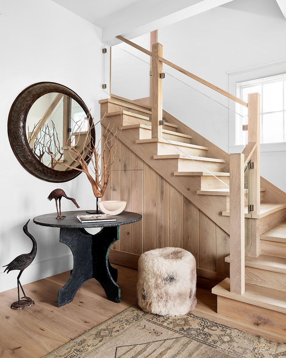 Beach style entry to the bungalow with a vintage console table, round mirror and staircase leading to the upper level