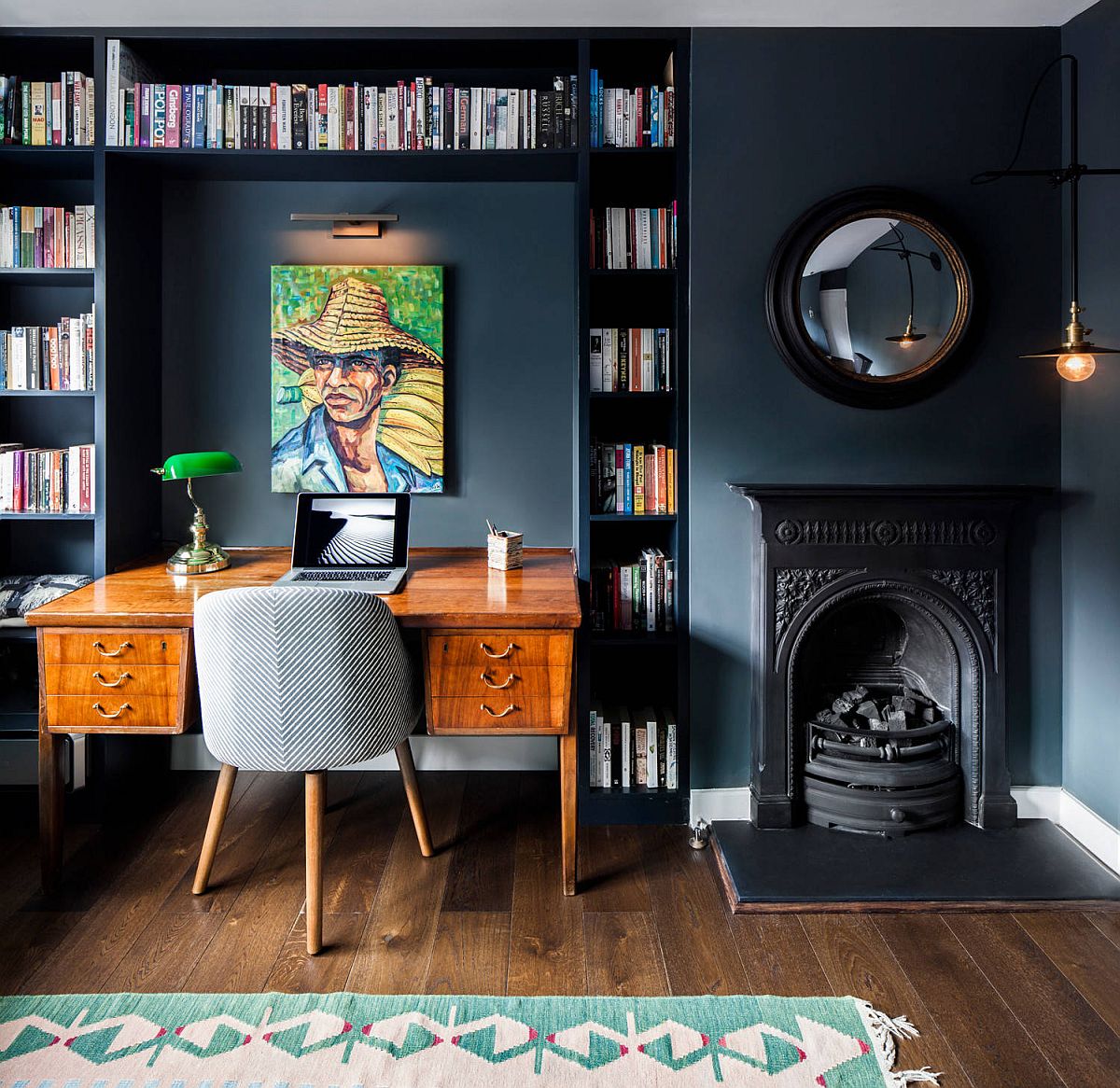 Bookshelves around the desk in the dark bluish-gray eclectic home office make an impact