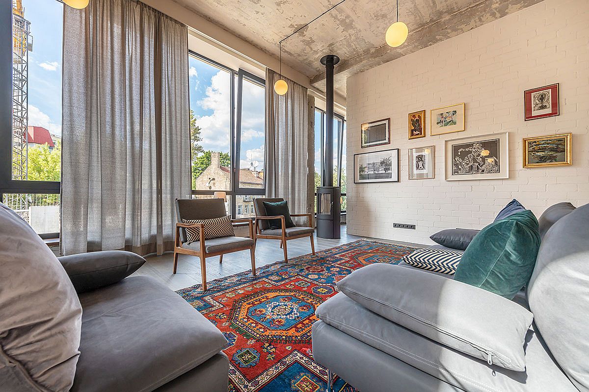 Brick wall that is painted white acts as gallery wall in the modern industrial living room with a lovely, colorful rug