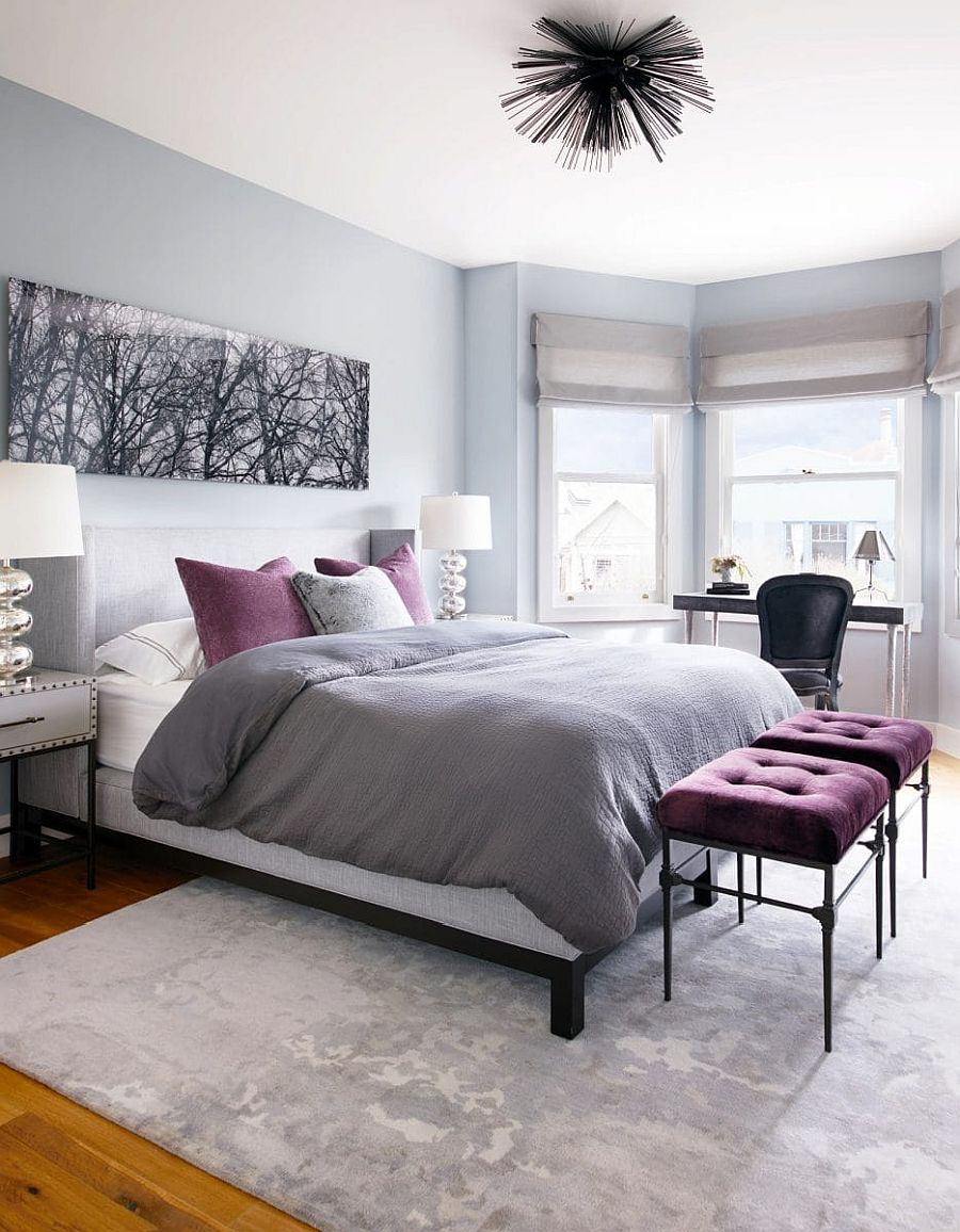 Splashes of purple ushered in by throw pillows and tufted stools uplift the bedroom in gray and white