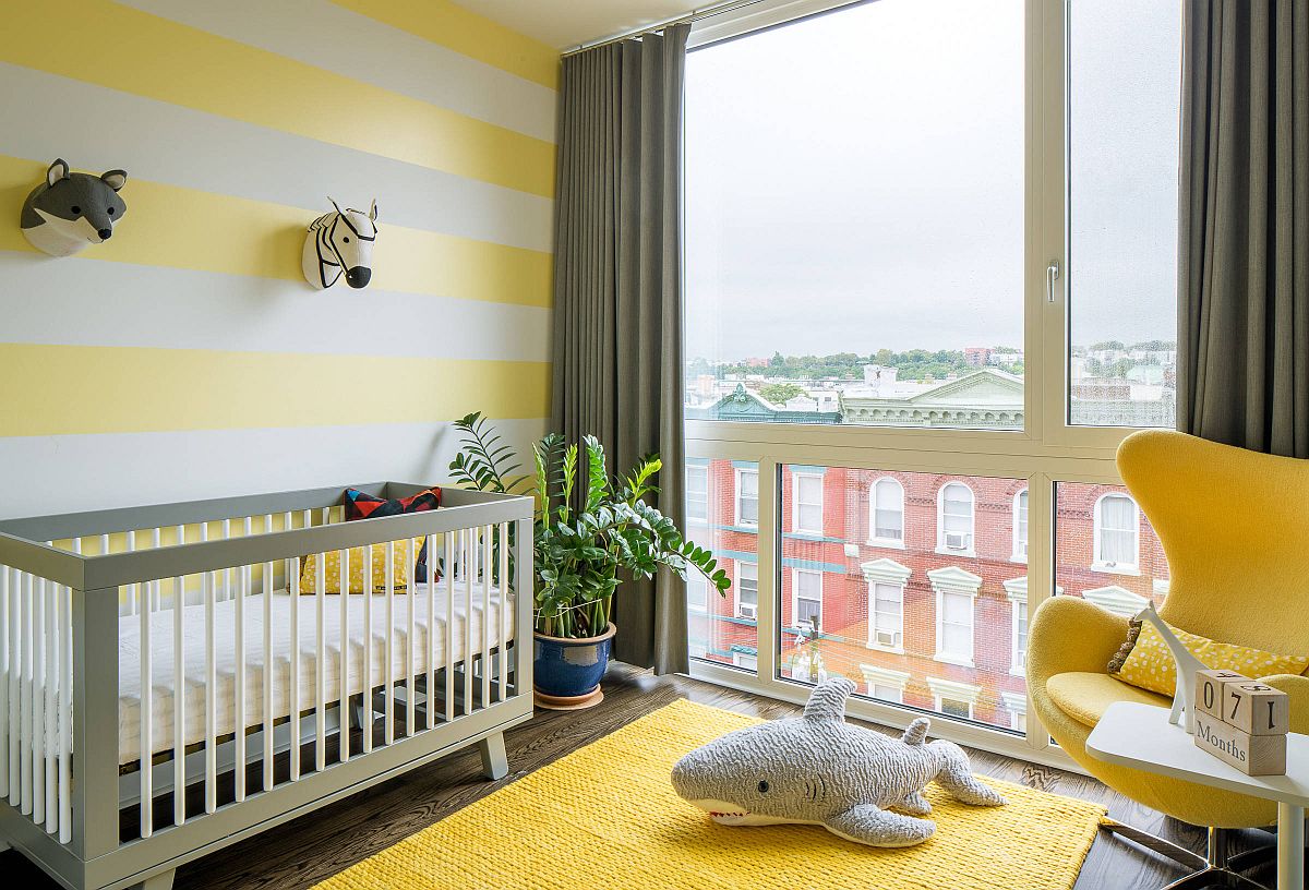 Striped accent wall in yellow and white along with yellow rug and chair in the smart modern nursery