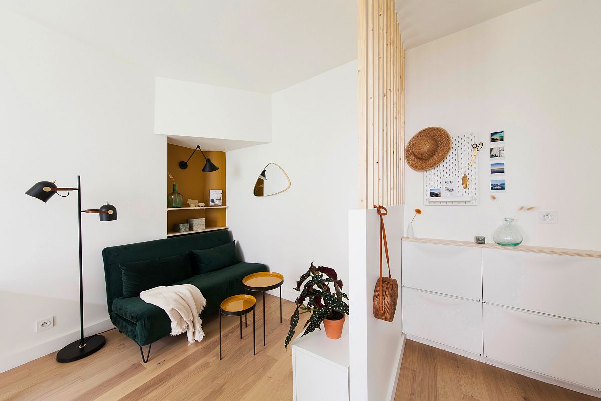 Tiny open living area of the Scandinavian style home with dark green sofa that seats two