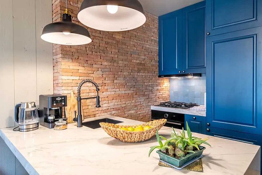 Apartment kitchen with blue cabinets and exposed brick wall section along with dashing pendant lights