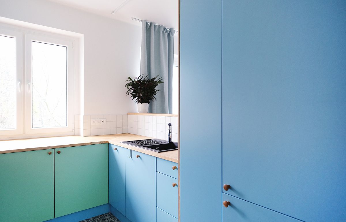 Blue and sea green cabinets add color to the adaptable kitchen of the apartment in white