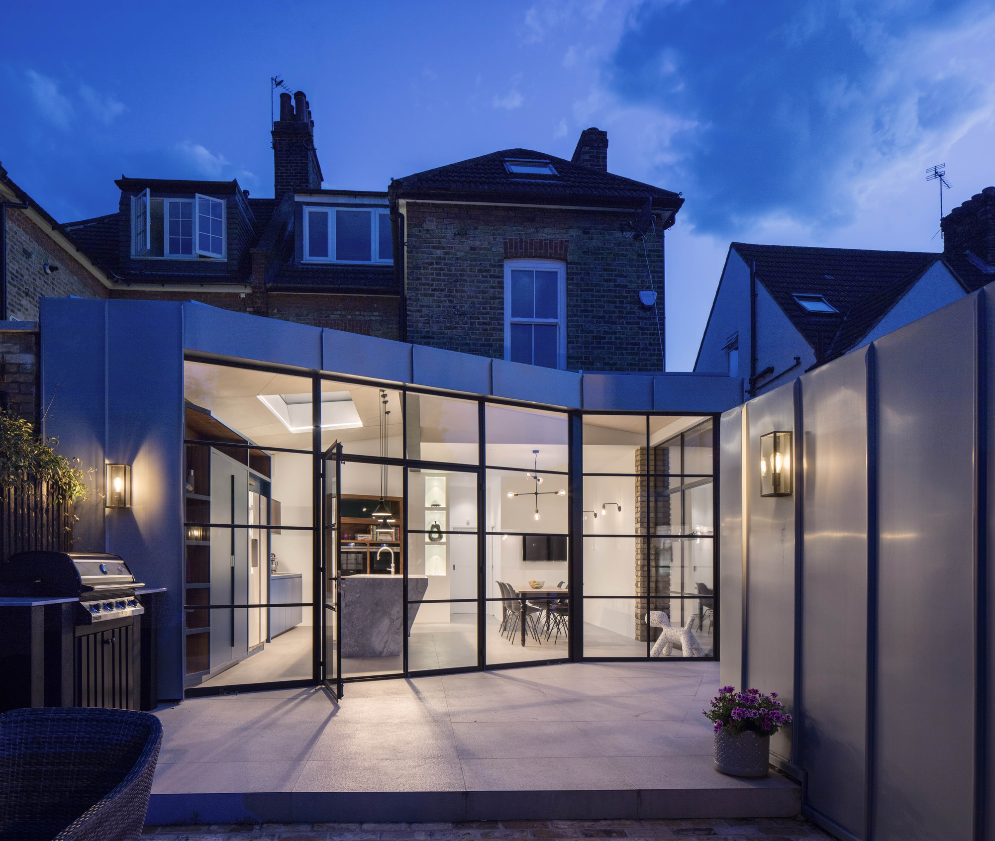 Dark-framed glass walls connect the kitchen and dining area with the garden