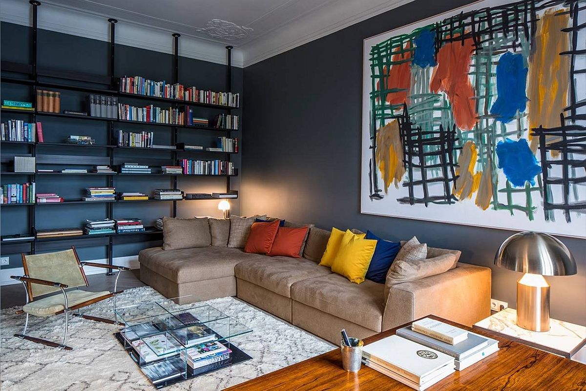 Gorgeous home library with deep gray walls still feels cheerful thanks to the colorful wall art and accent pillows