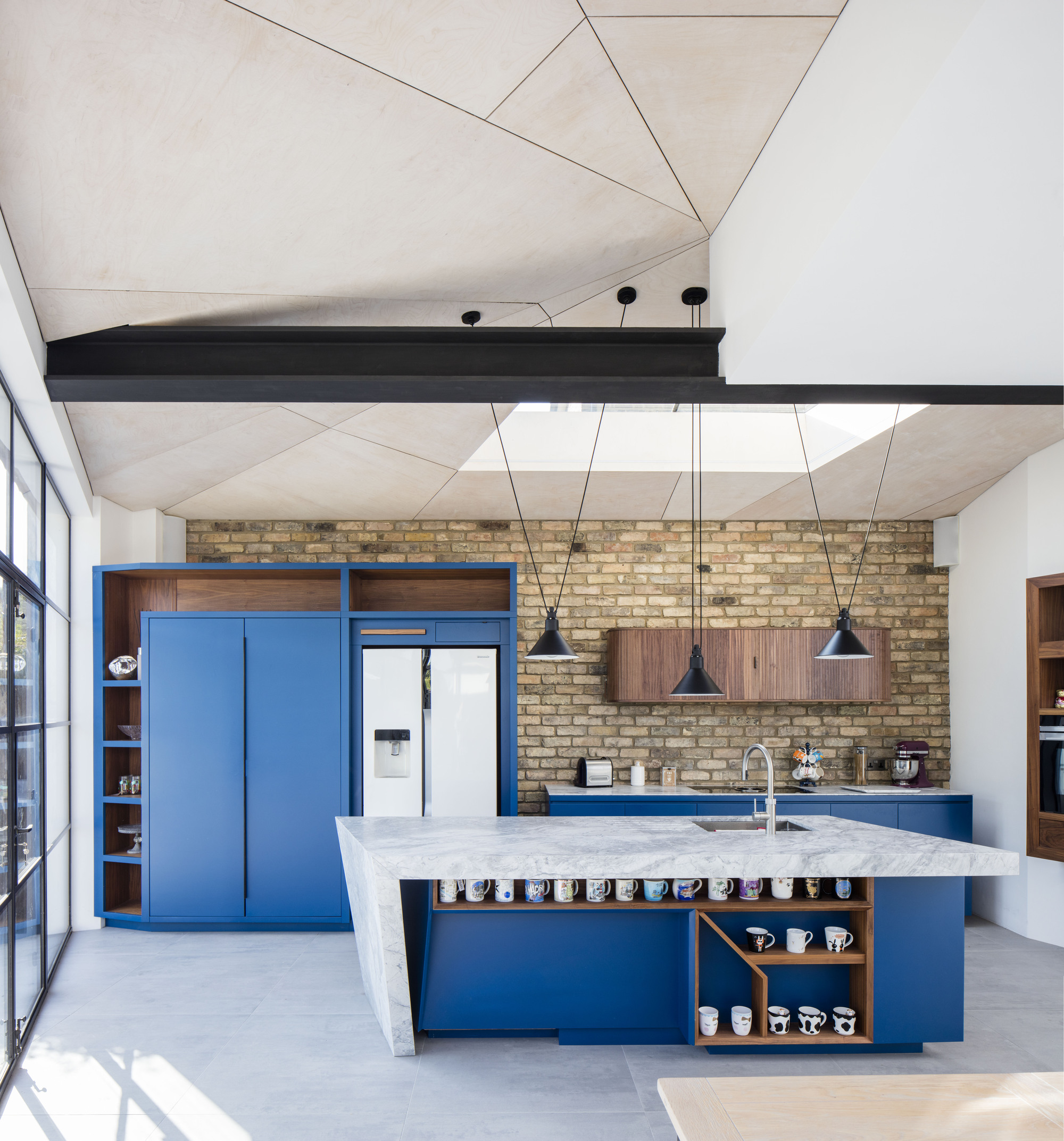 New kitchen of renovated family home in London with brick wall backdrop and blue cabinets