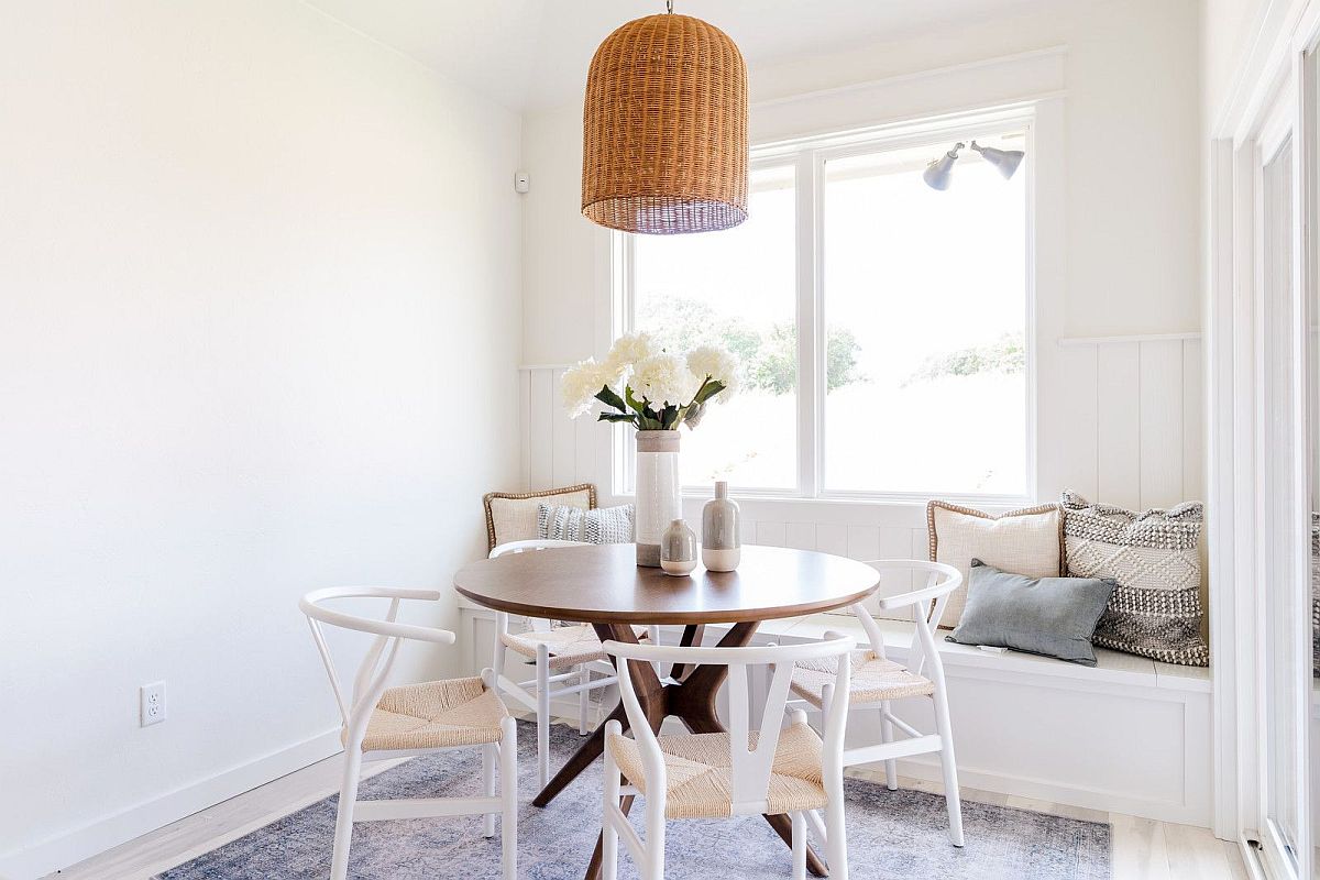 Small white dining room with round dining table, chairs and a comfy window seat in the backdrop